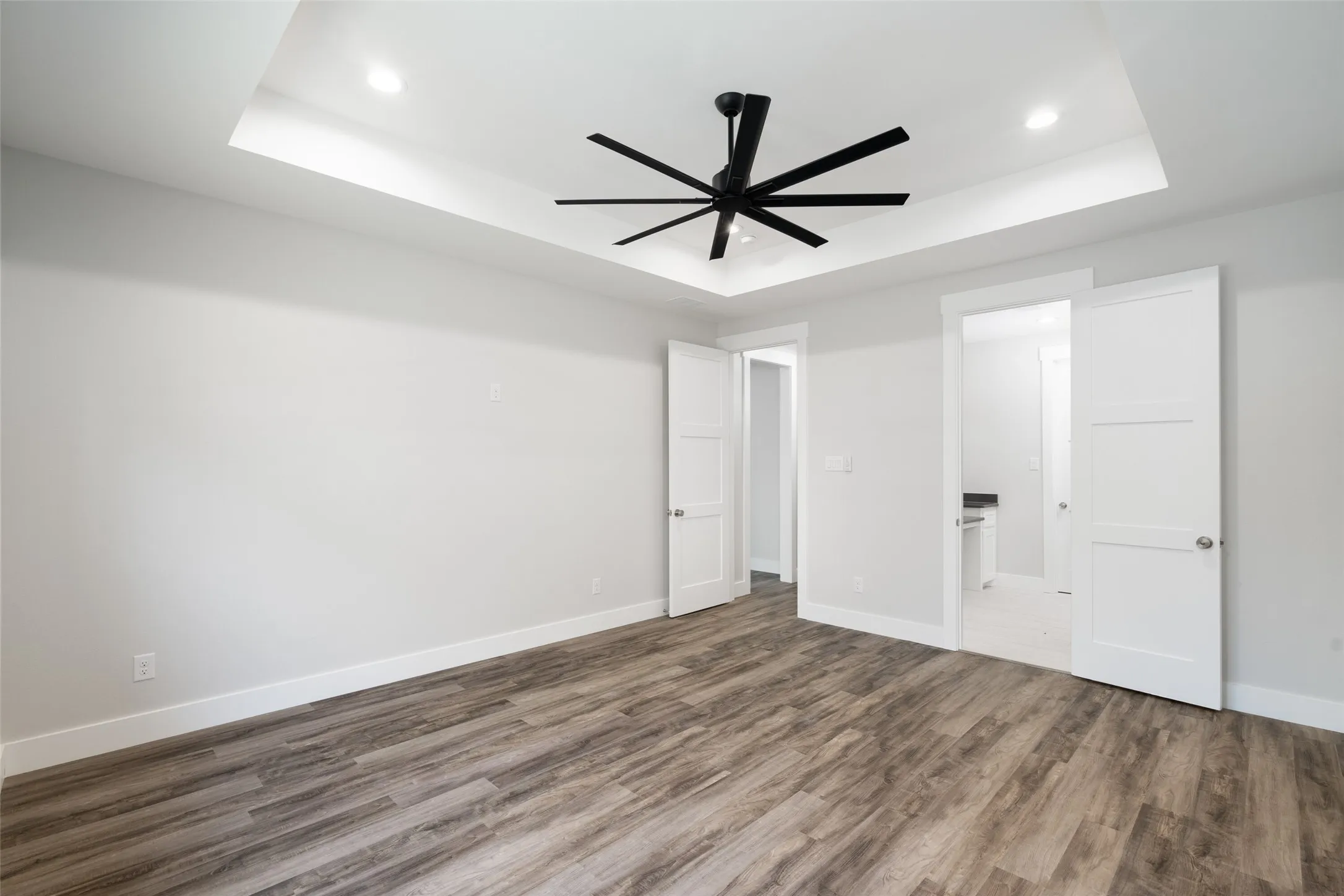 Unfurnished bedroom featuring a tray ceiling, connected bathroom, ceiling fan, and wood-type flooring