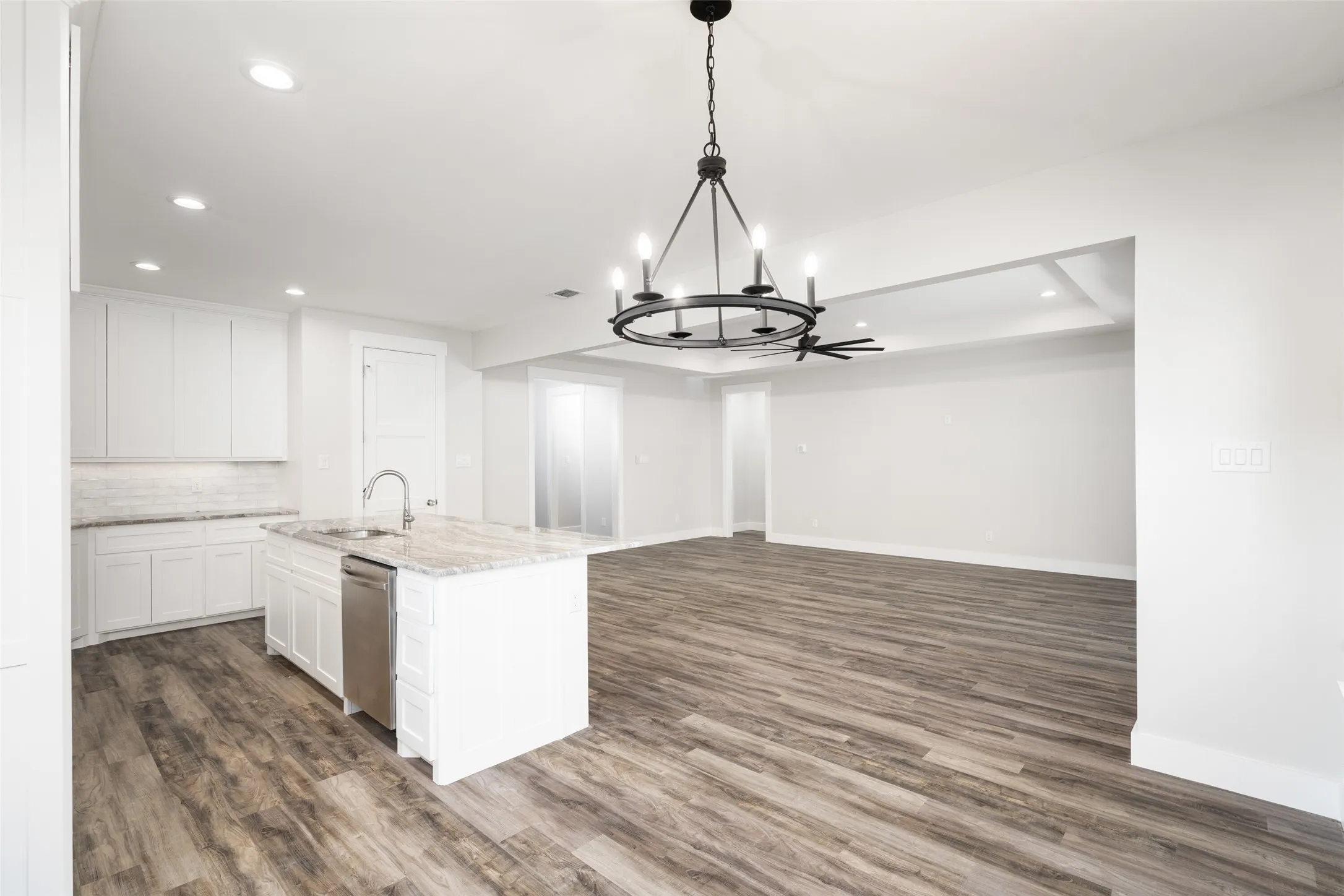 Kitchen featuring pendant lighting, white cabinets, a center island with sink, sink, and light stone countertops