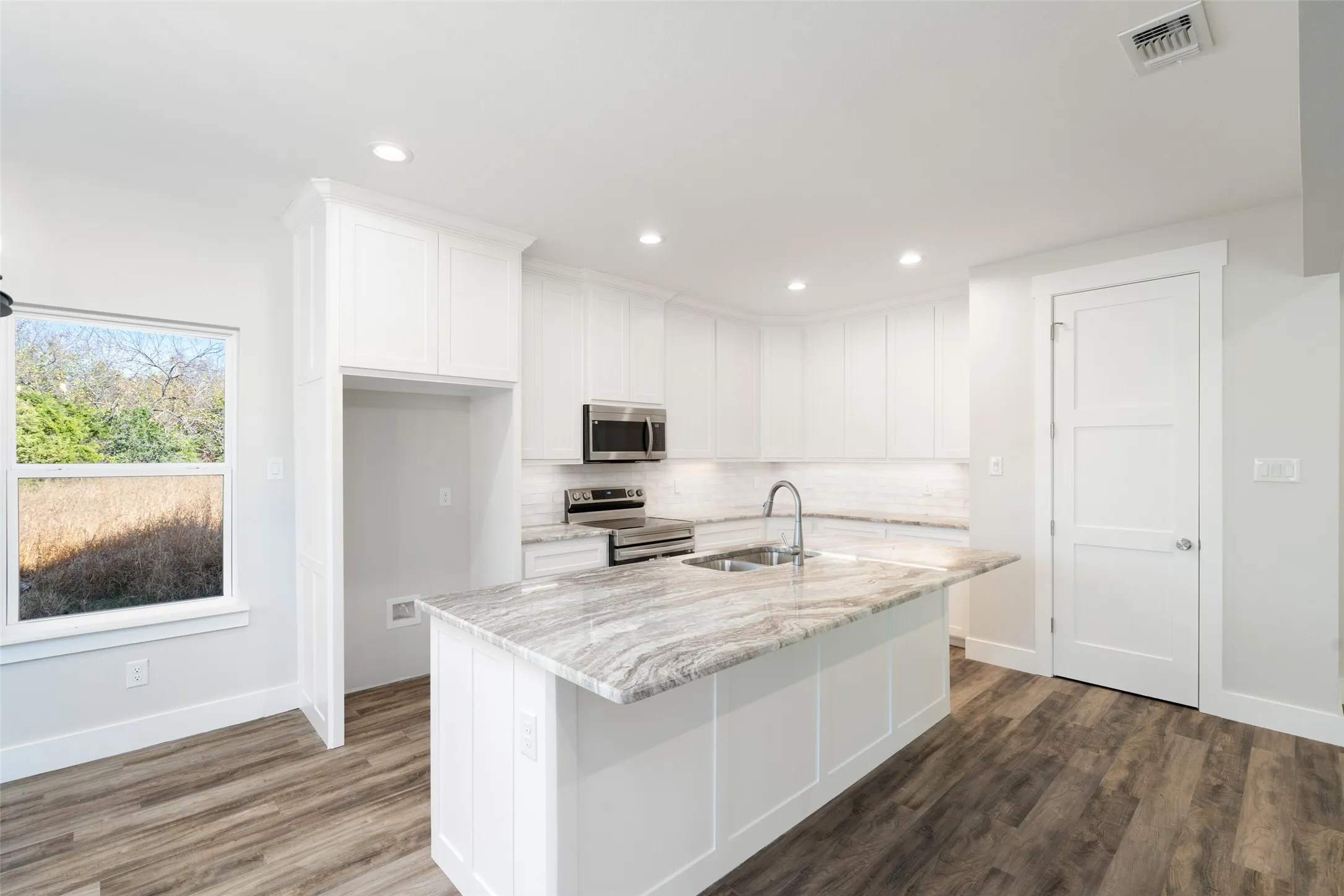 Kitchen with sink, light stone counters, a center island with sink, white cabinets, and appliances with stainless steel finishes
