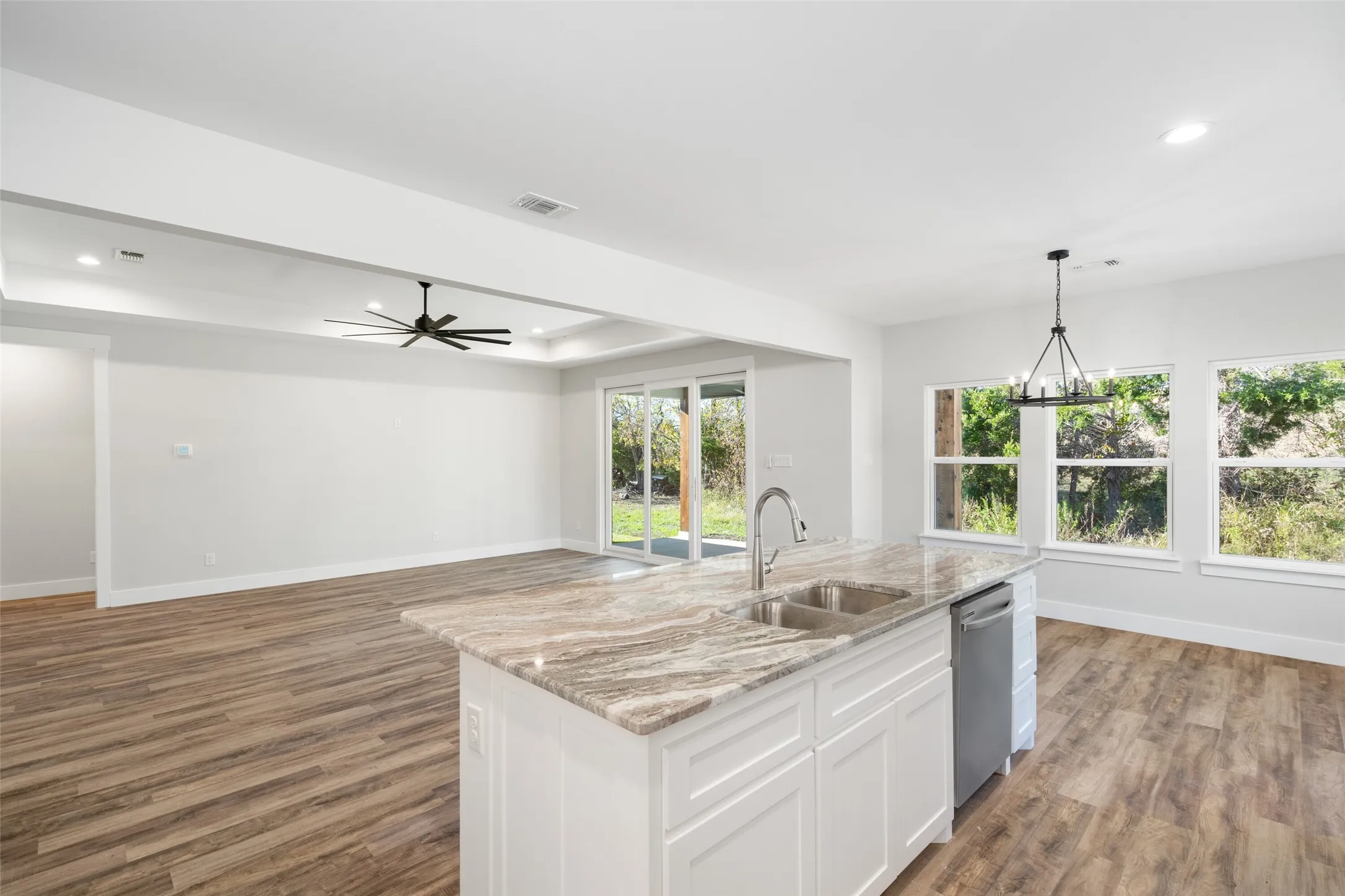 Kitchen with dishwasher, a kitchen island with sink, sink, light stone counters, and white cabinetry