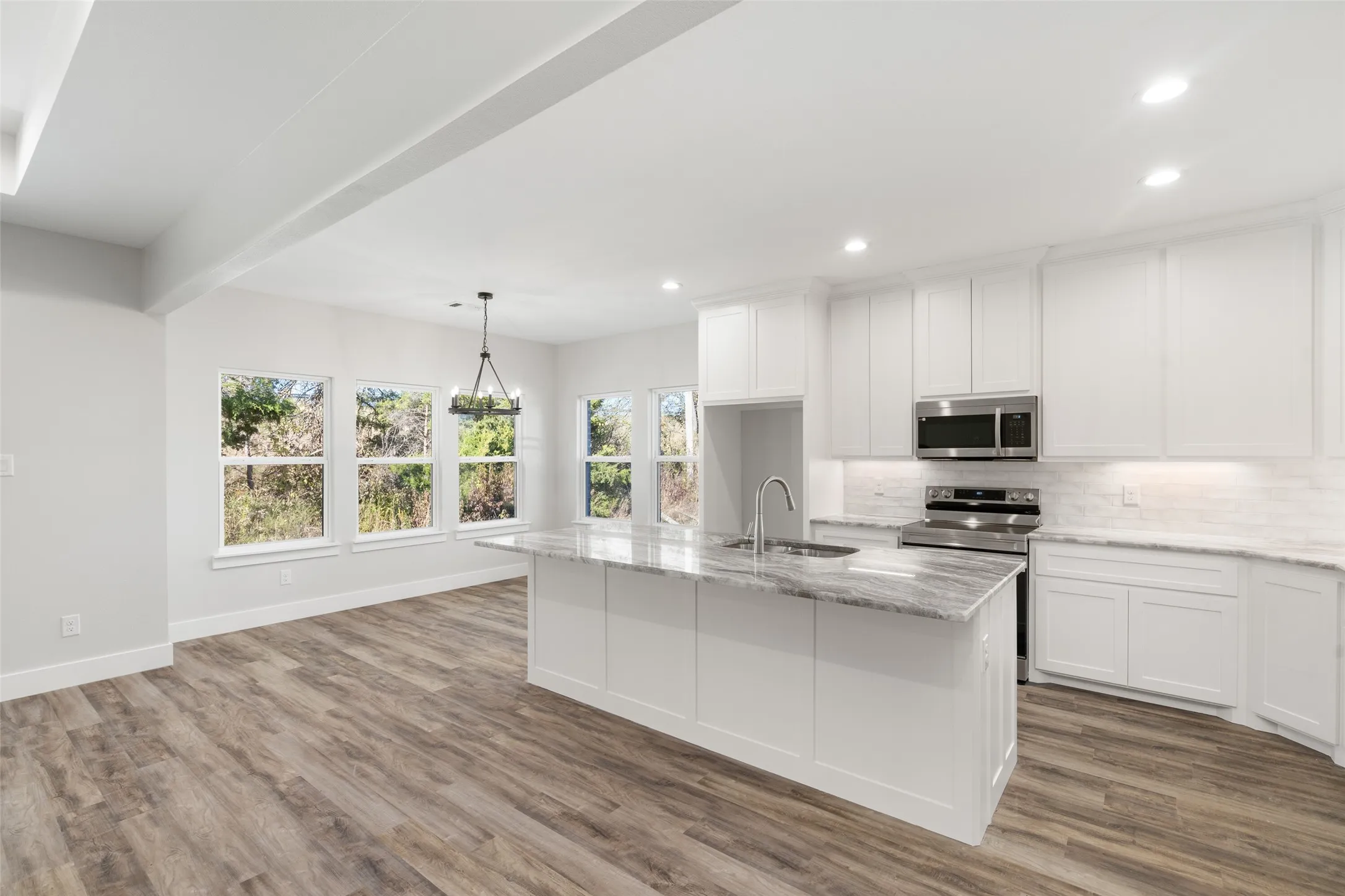 Kitchen with light stone countertops, stainless steel appliances, a kitchen island with sink, pendant lighting, and white cabinetry