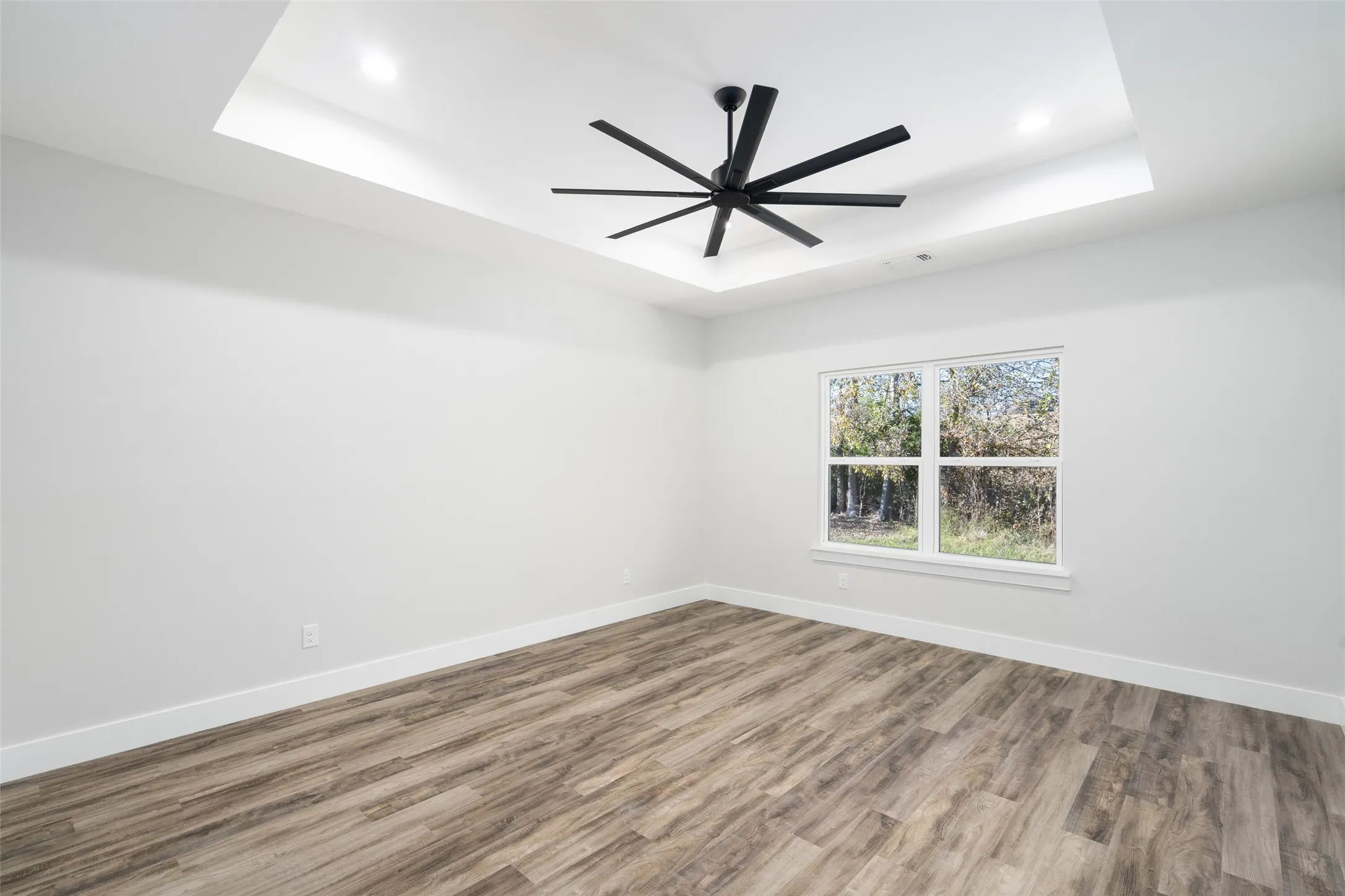 Empty room featuring hardwood / wood-style floors, ceiling fan, and a tray ceiling