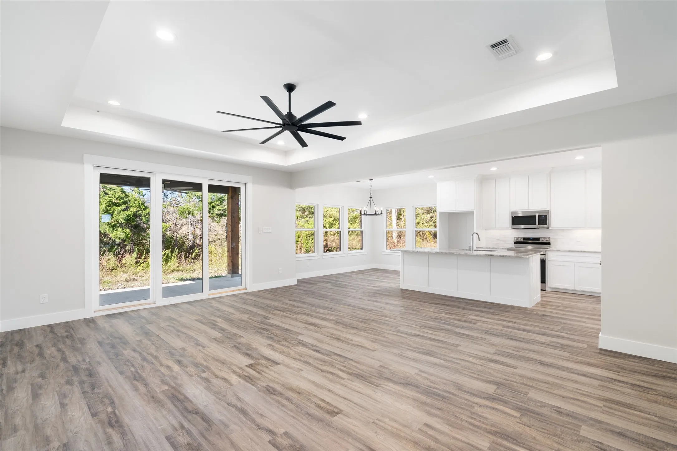 Unfurnished living room featuring ceiling fan with notable chandelier, a raised ceiling, sink, and light hardwood / wood-style flooring