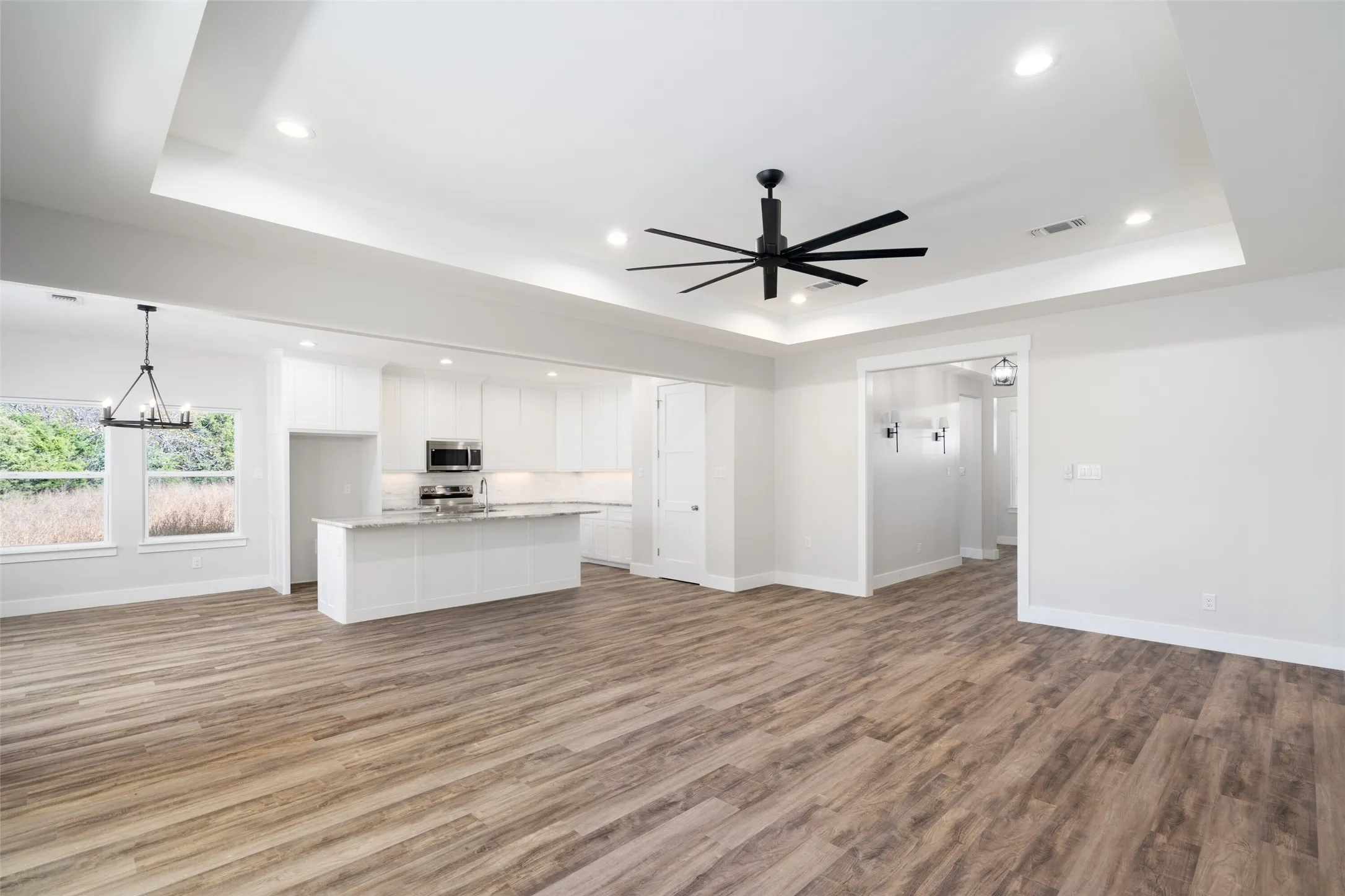 Unfurnished living room with a raised ceiling, light hardwood / wood-style floors, and ceiling fan with notable chandelier