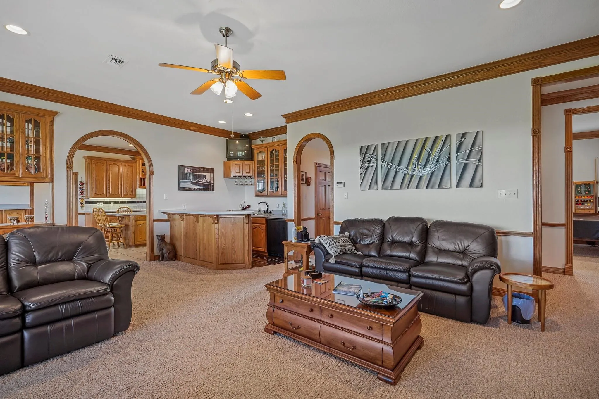 Carpeted living room featuring ceiling fan, sink, and ornamental molding