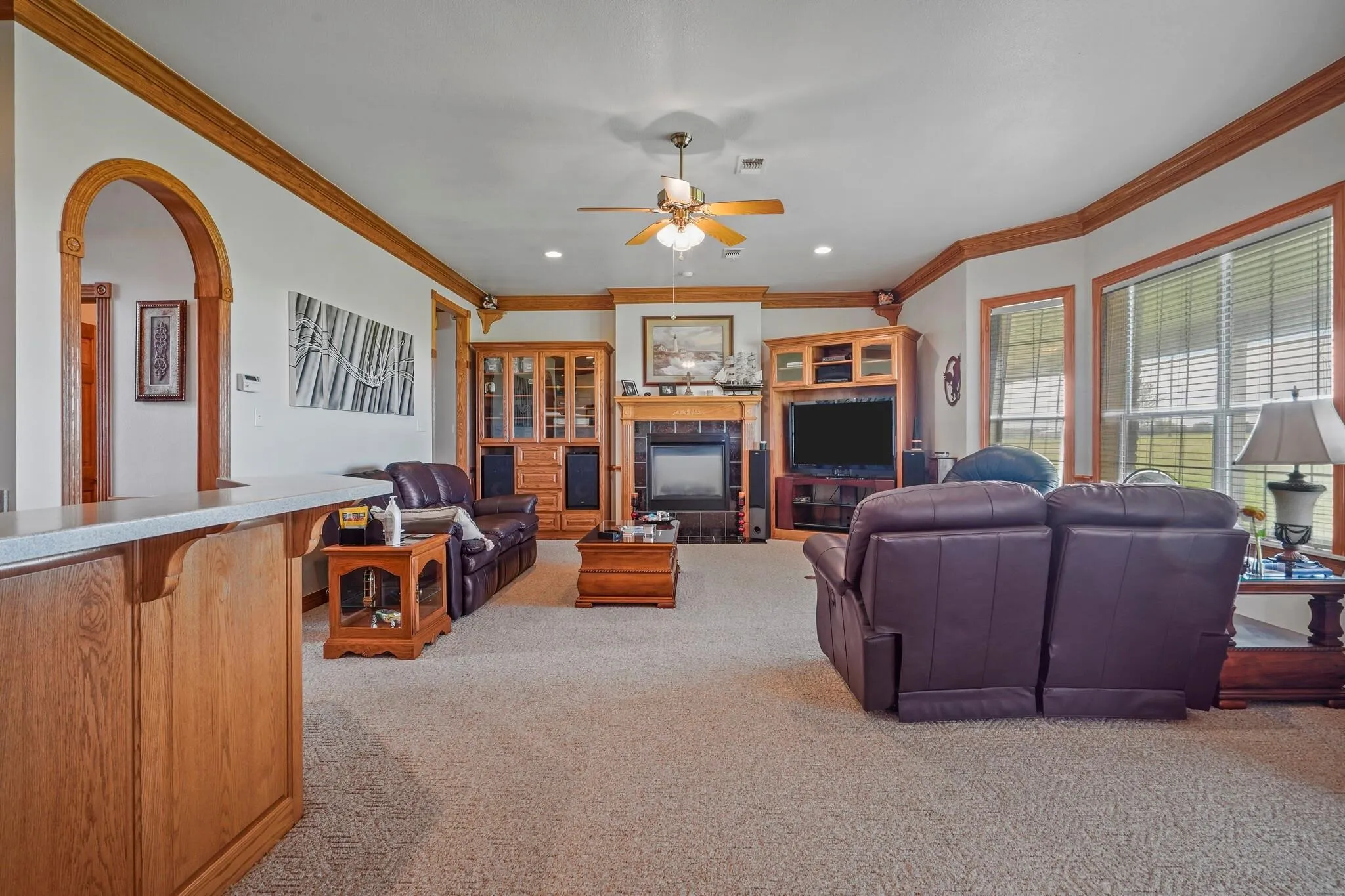 Carpeted living room with a tiled fireplace, crown molding, and ceiling fan