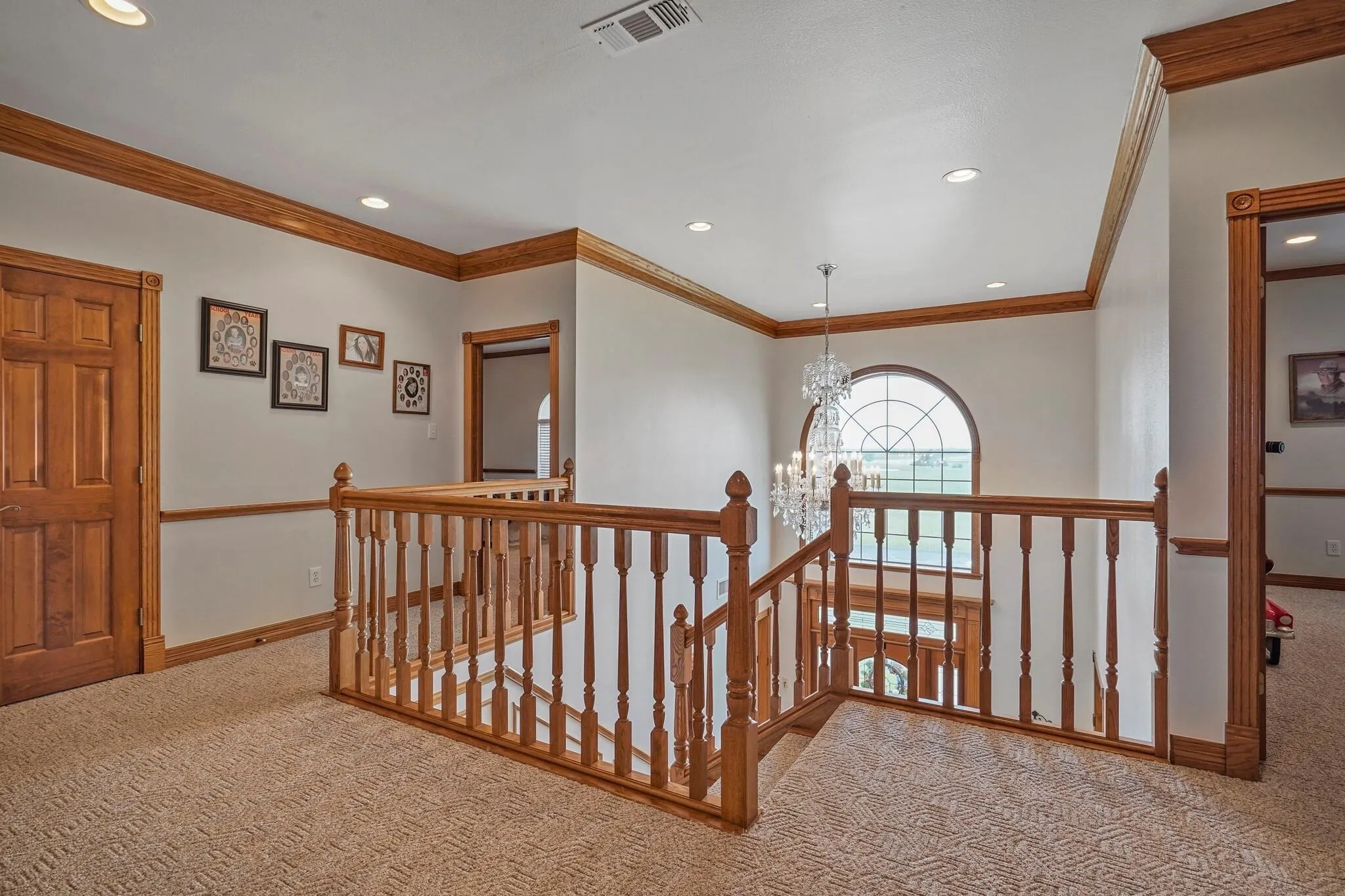 Hallway with ornamental molding, light carpet, and an inviting chandelier