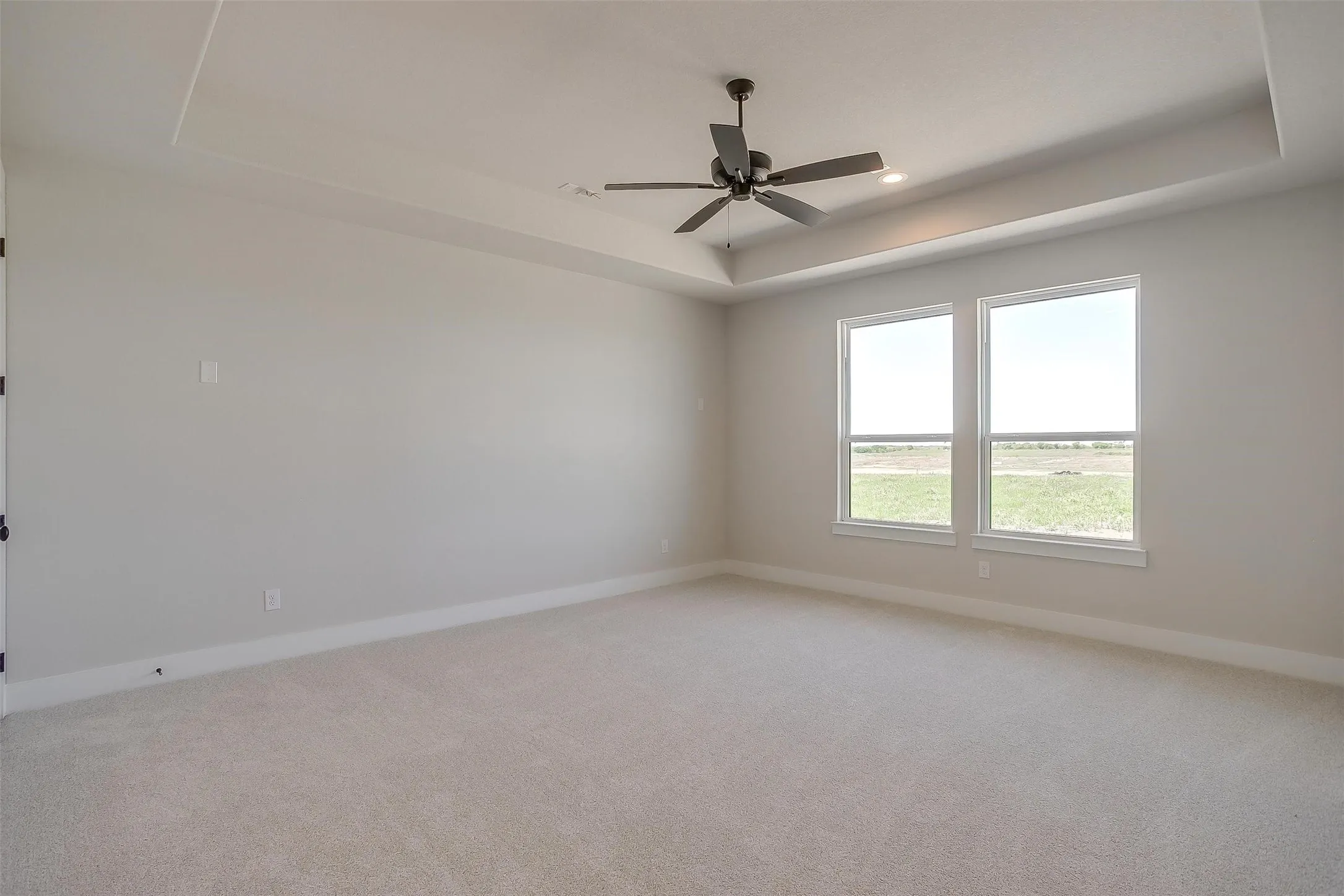 Spare room featuring a tray ceiling, baseboards, ceiling fan, and light carpet