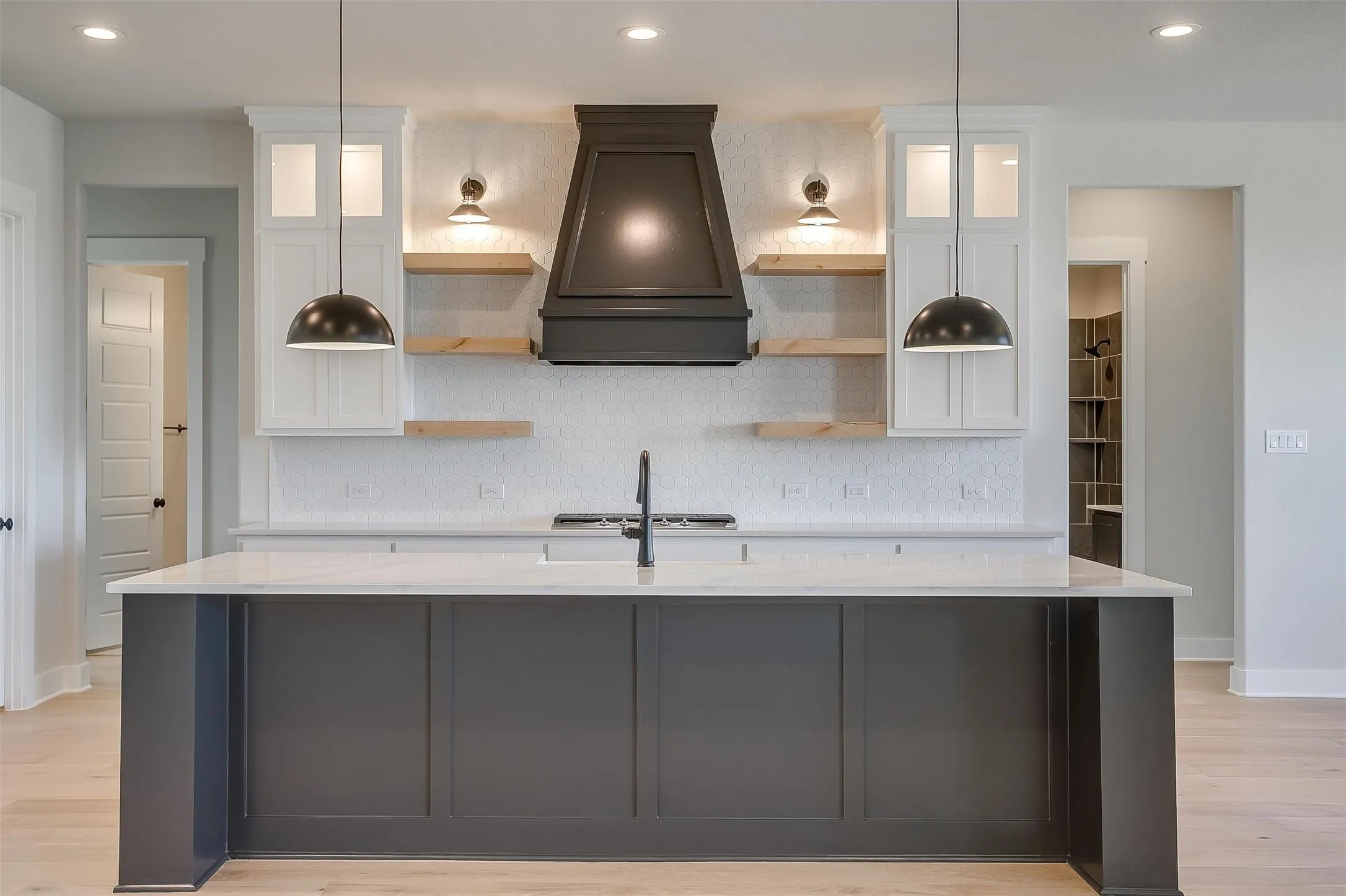 Kitchen featuring backsplash, open shelves, premium range hood, and an island with sink