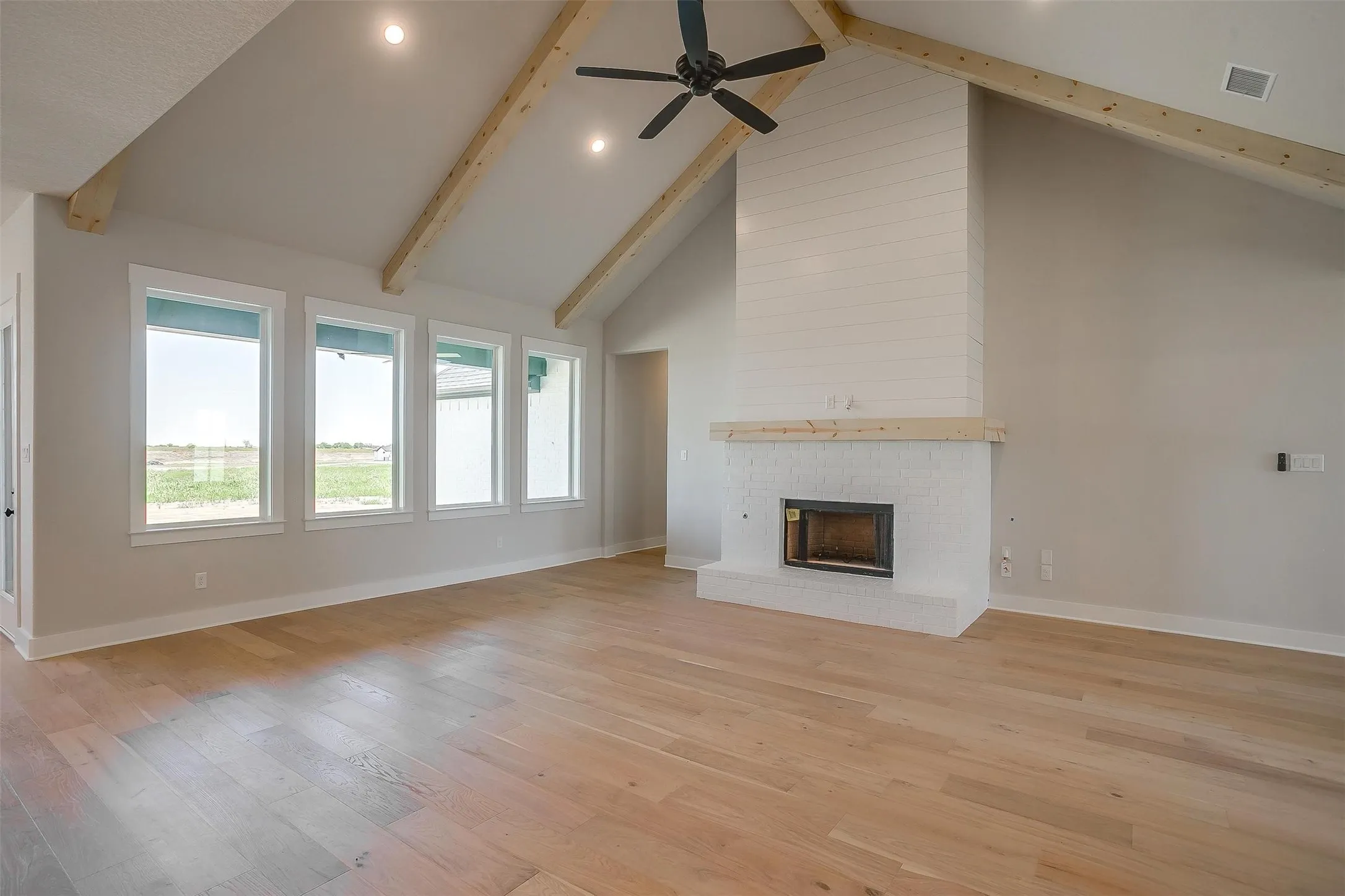 Unfurnished living room featuring visible vents, a brick fireplace, beamed ceiling, light wood finished floors, and high vaulted ceiling