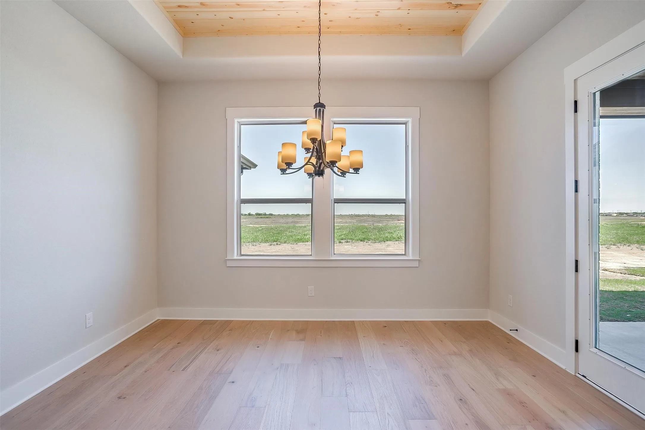 Unfurnished room with light wood-type flooring, a raised ceiling, an inviting chandelier, and baseboards