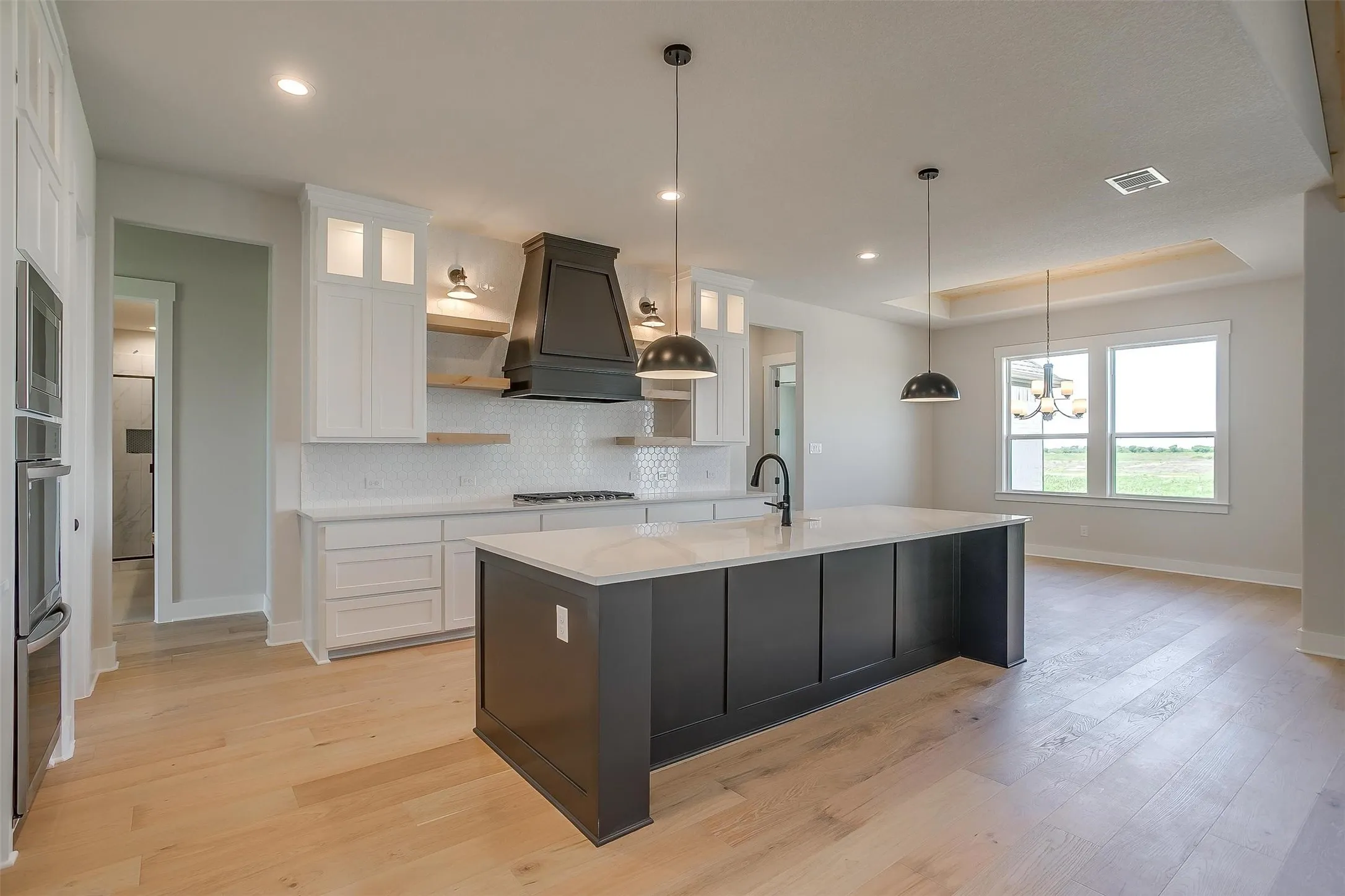 Kitchen featuring custom range hood, open shelves, white cabinets, visible vents, and stainless steel appliances