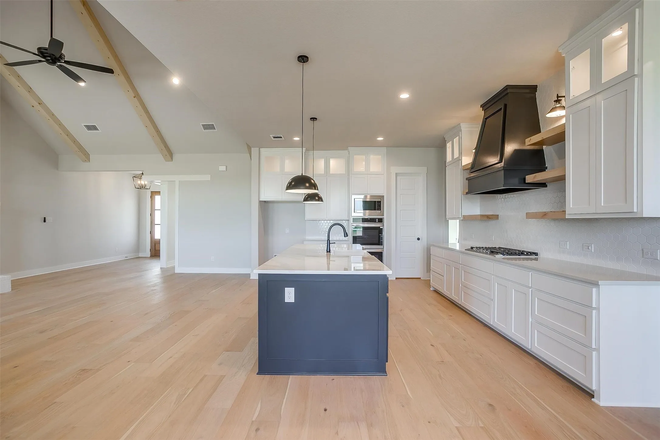 Kitchen with light wood-style floors, appliances with stainless steel finishes, light countertops, premium range hood, and decorative backsplash