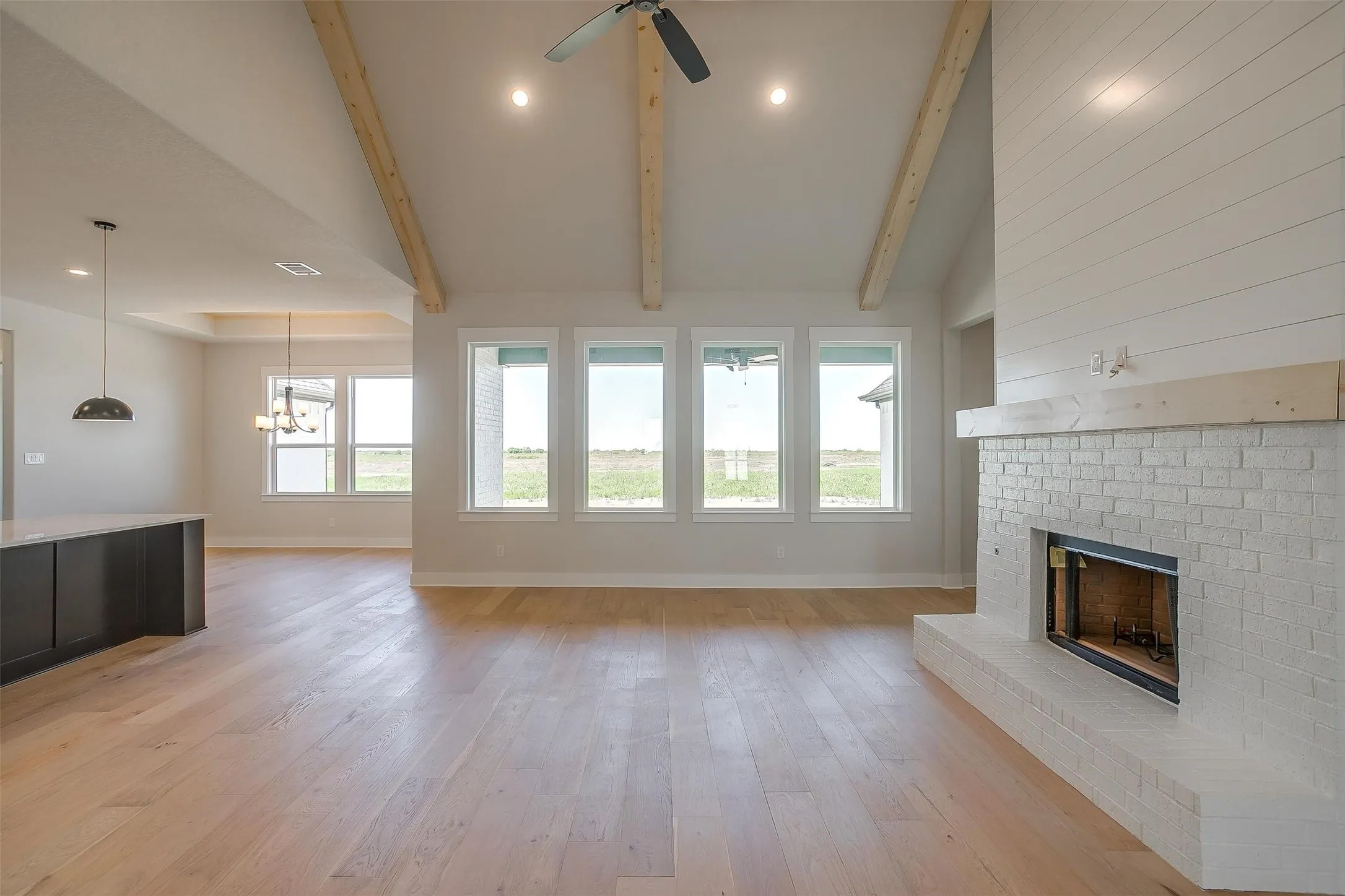 Unfurnished living room featuring ceiling fan with notable chandelier, beamed ceiling, a fireplace, light wood-style flooring, and baseboards