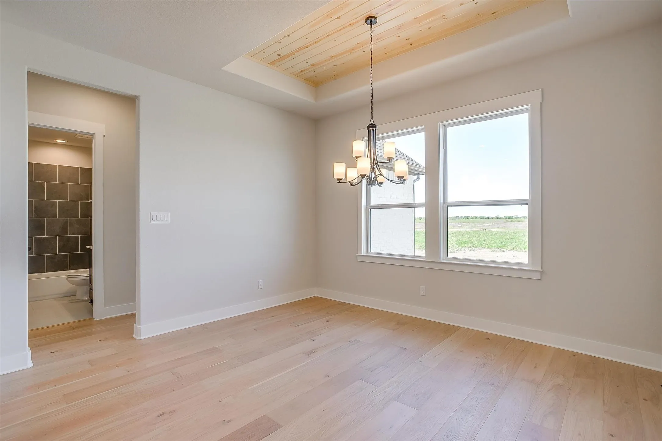 Unfurnished room with a tray ceiling, light wood-style flooring, a chandelier, and baseboards