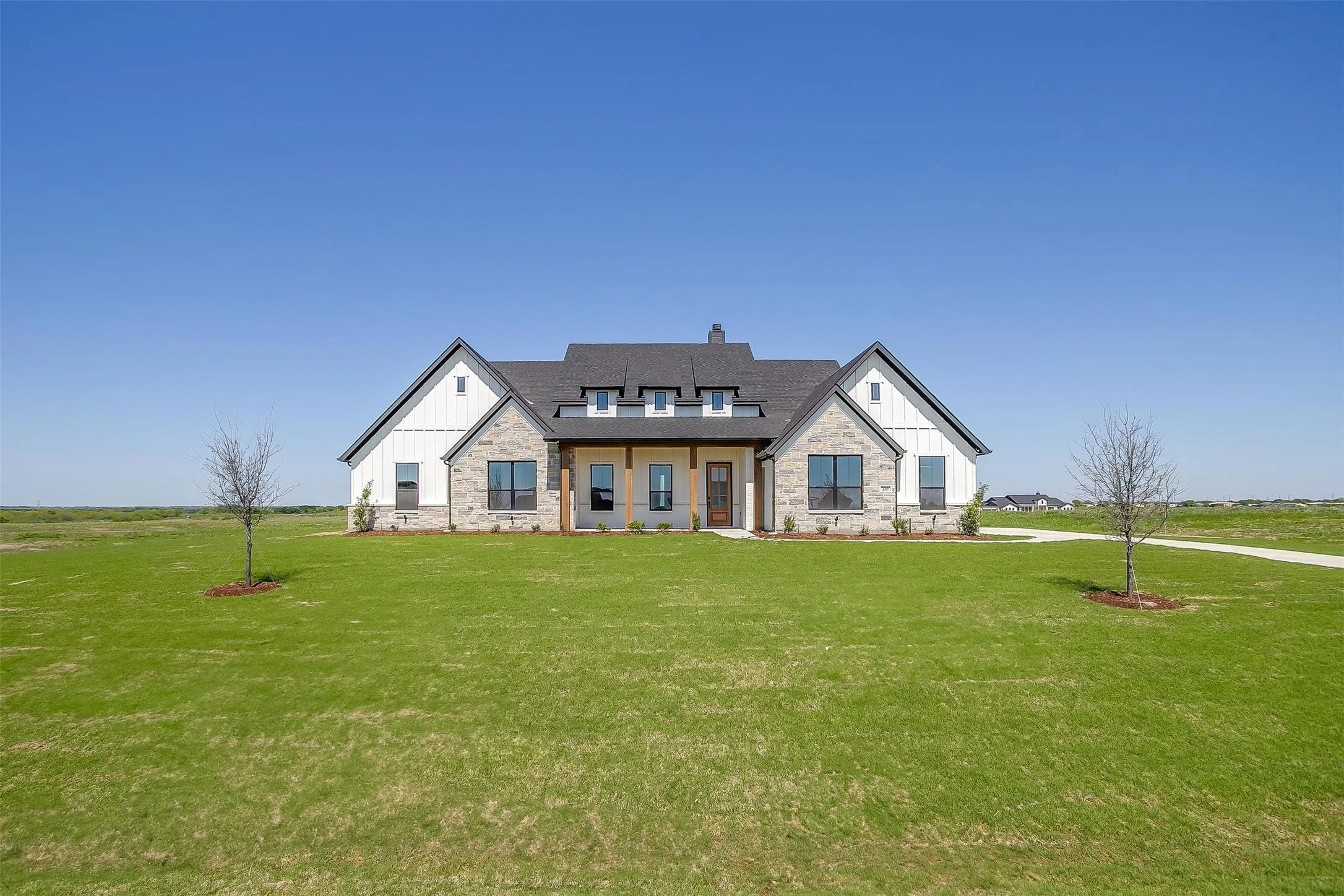 Modern inspired farmhouse with roof with shingles, a chimney, board and batten siding, stone siding, and a front lawn