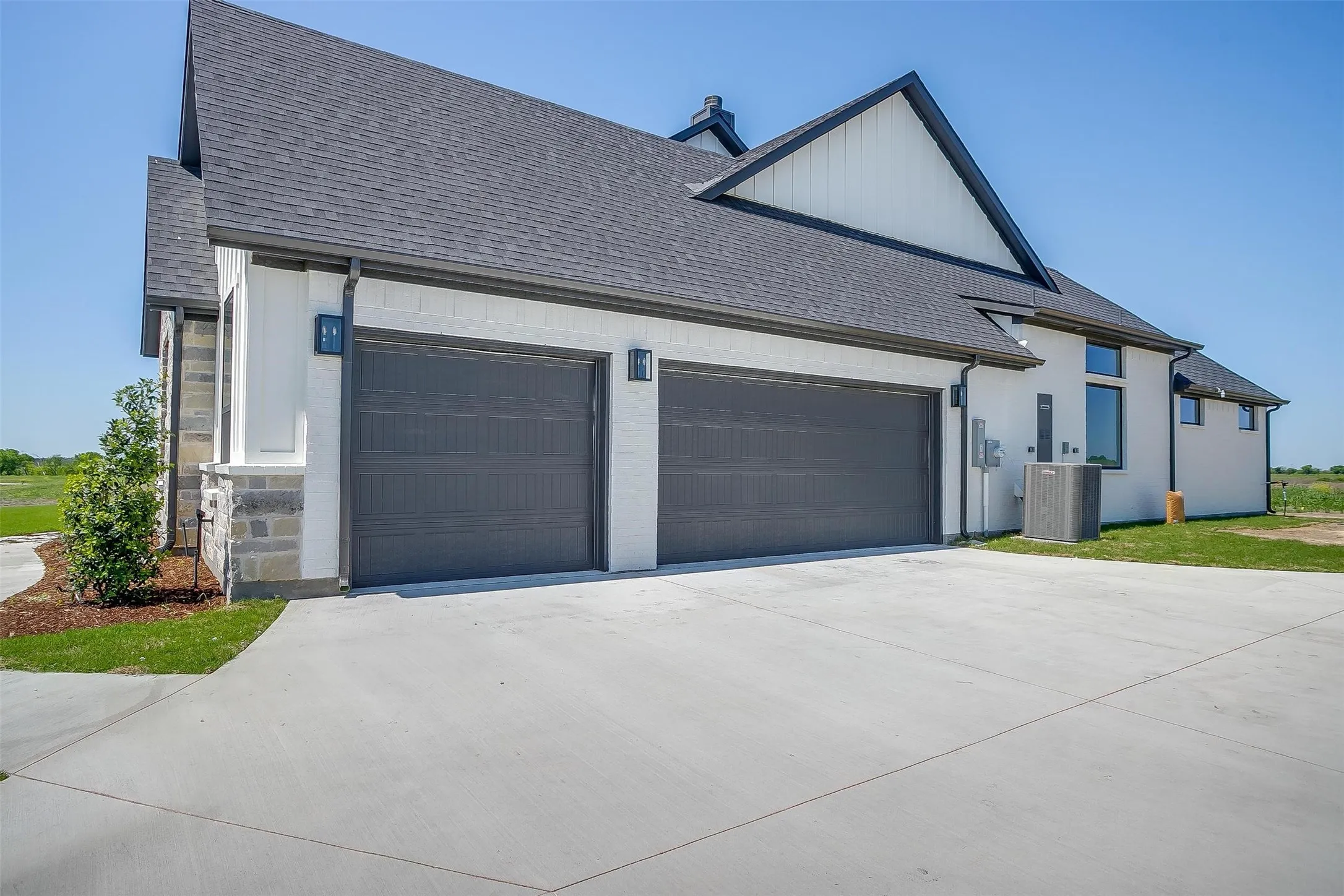View of side of home with roof with shingles, driveway, central AC unit, and an attached garage