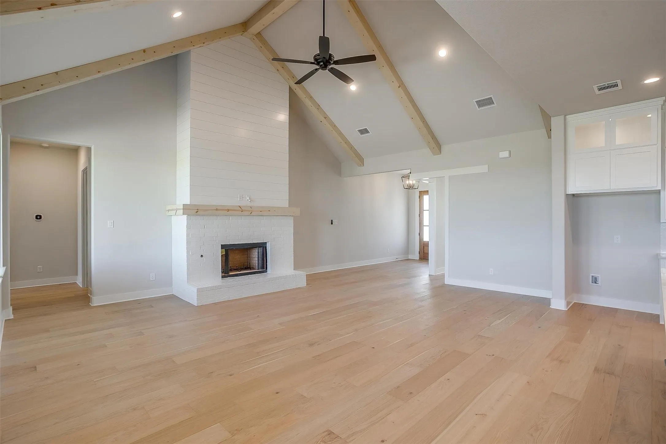 Unfurnished living room with visible vents, light wood-style flooring, a ceiling fan, and a brick fireplace
