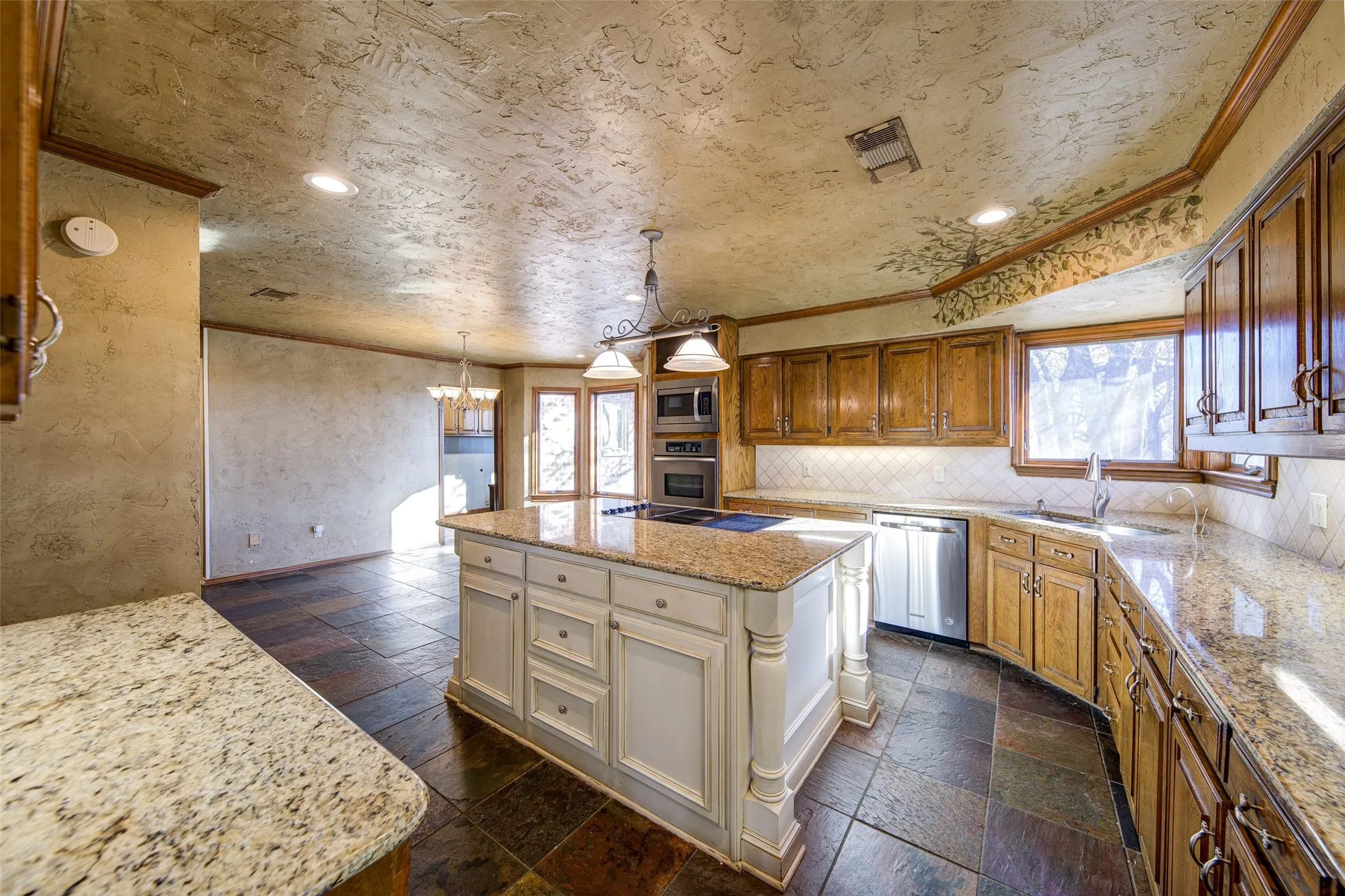 Kitchen featuring appliances with stainless steel finishes, stone tile floors, ornamental molding, decorative backsplash, and light stone counters