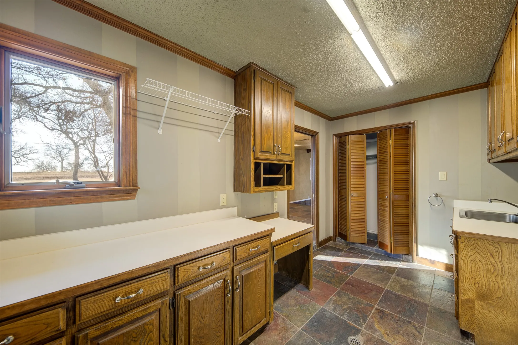 Kitchen featuring ornamental molding, stone tile floors, brown cabinets, light countertops, and a textured ceiling