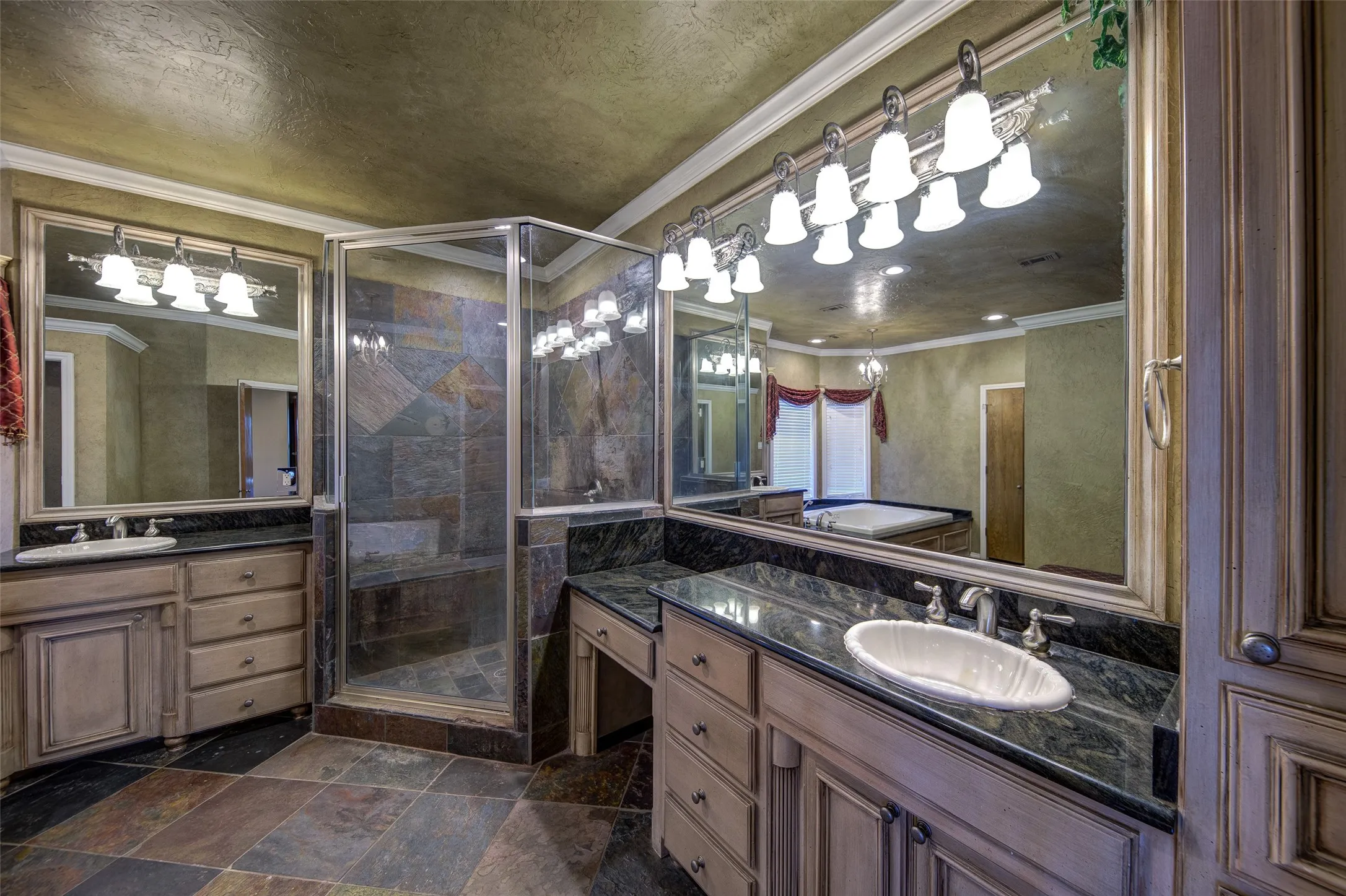 Bathroom with a stall shower, two vanities, crown molding, and stone finish floors