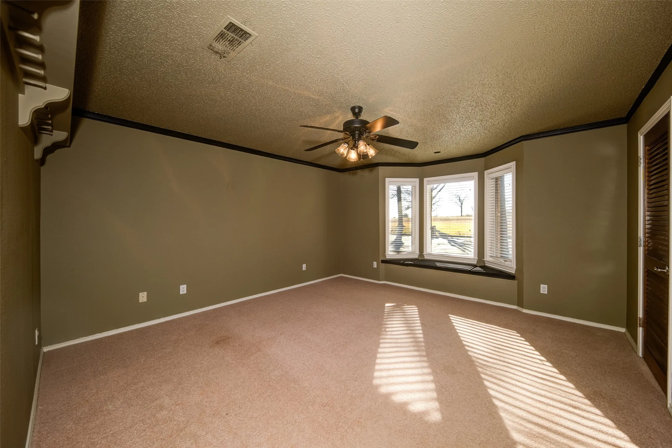 Unfurnished bedroom featuring carpet, ornamental molding, a textured ceiling, and a ceiling fan