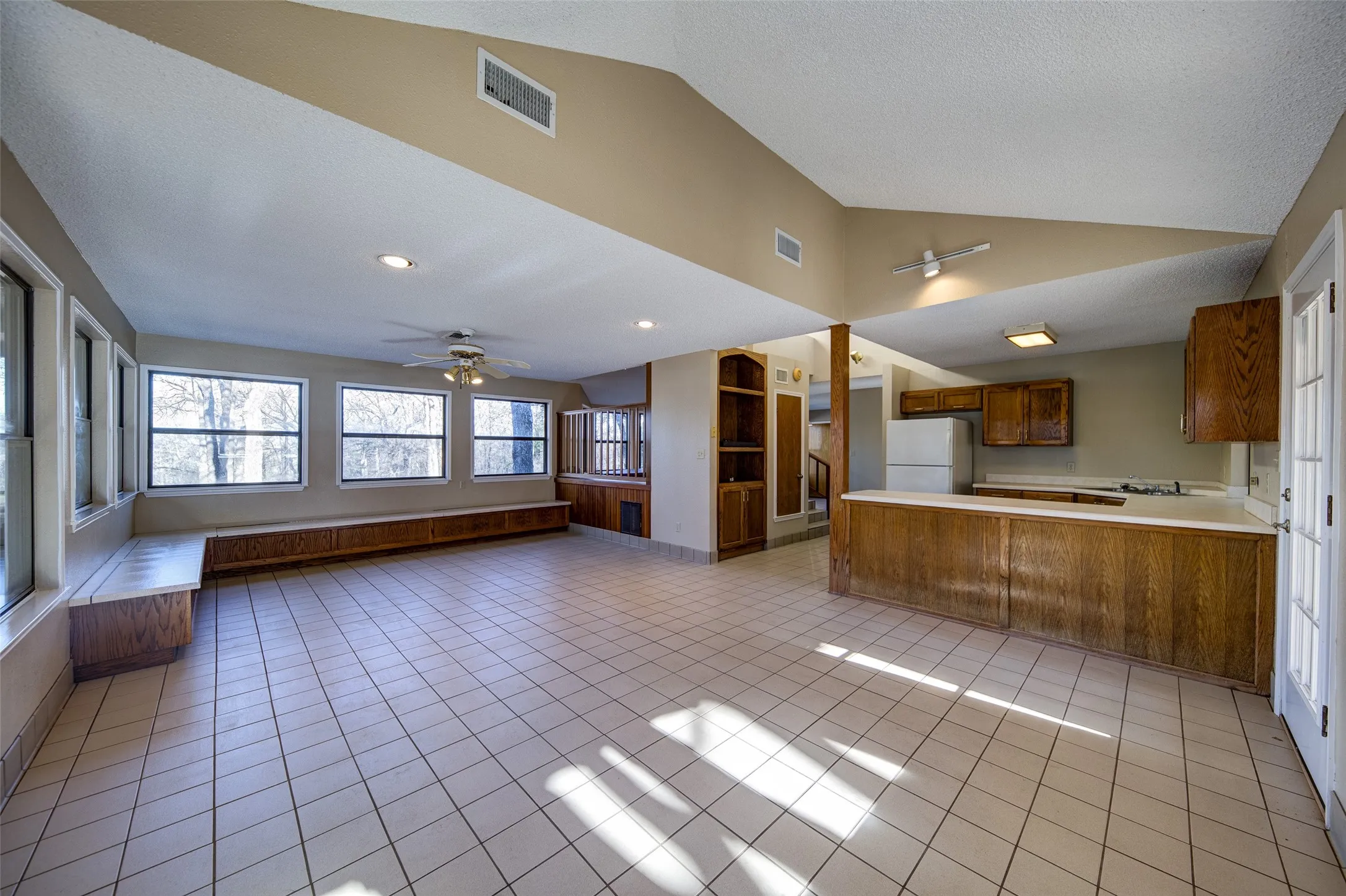 Kitchen featuring freestanding refrigerator, open floor plan, lofted ceiling, brown cabinetry, and light countertops