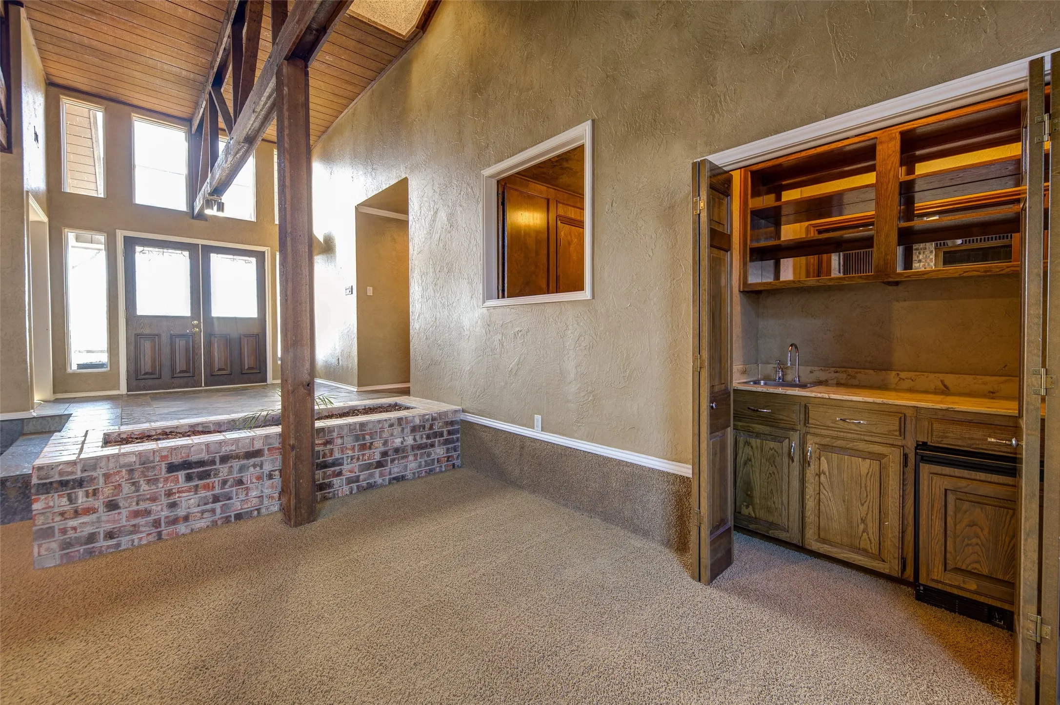 Carpeted foyer entrance featuring wooden ceiling, a textured wall, wet bar, and a towering ceiling