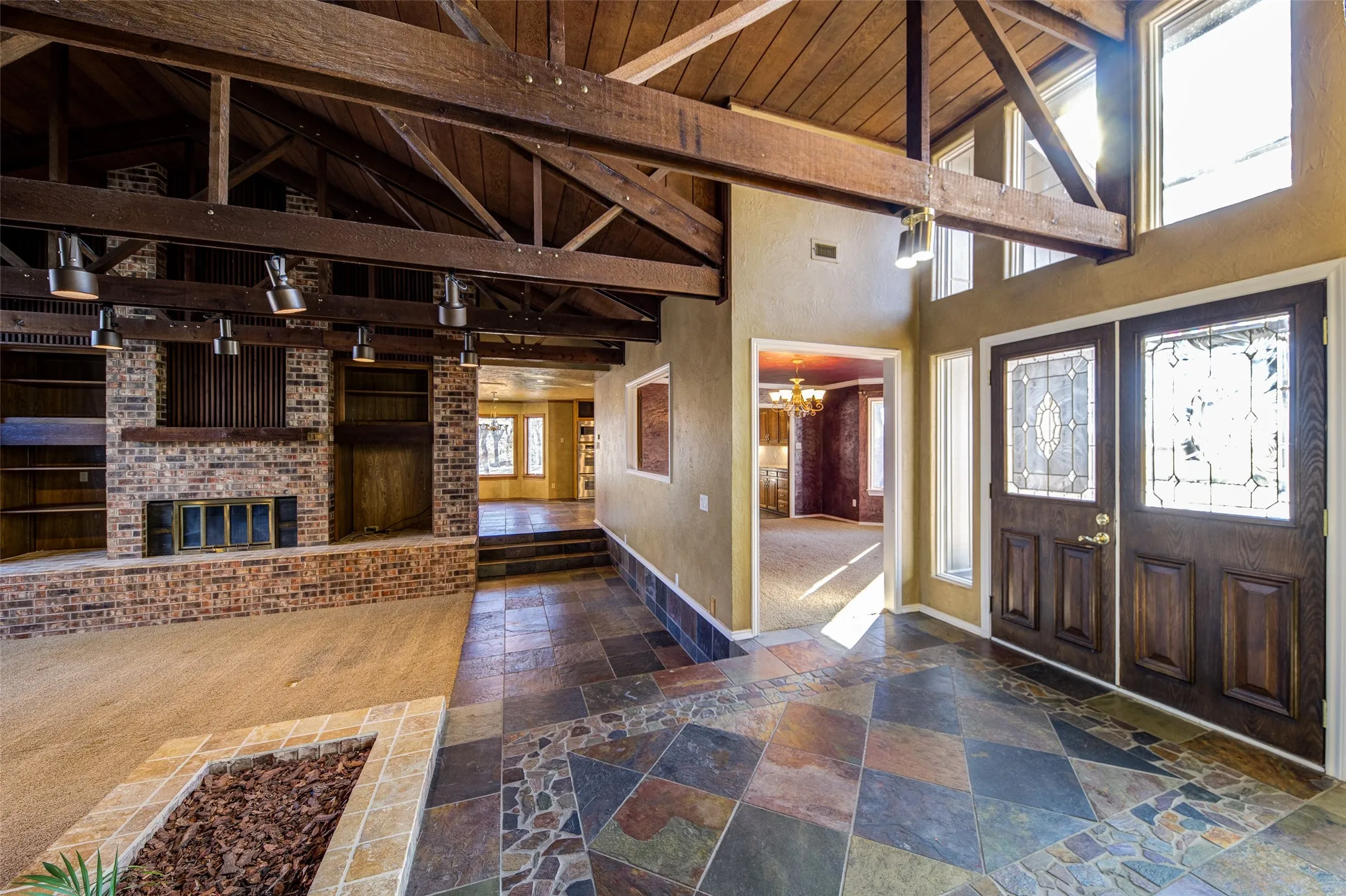 Entryway featuring stone tile floors, high vaulted ceiling, a chandelier, a wood ceiling with exposed beams, and a brick fireplace