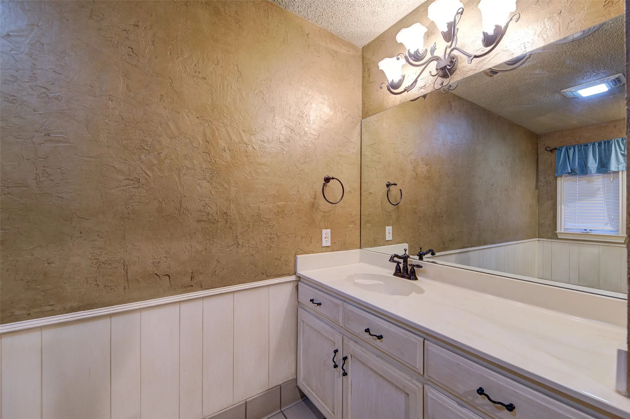 Bathroom featuring a textured ceiling, a chandelier, vanity, a wainscoted wall, and a decorative wall