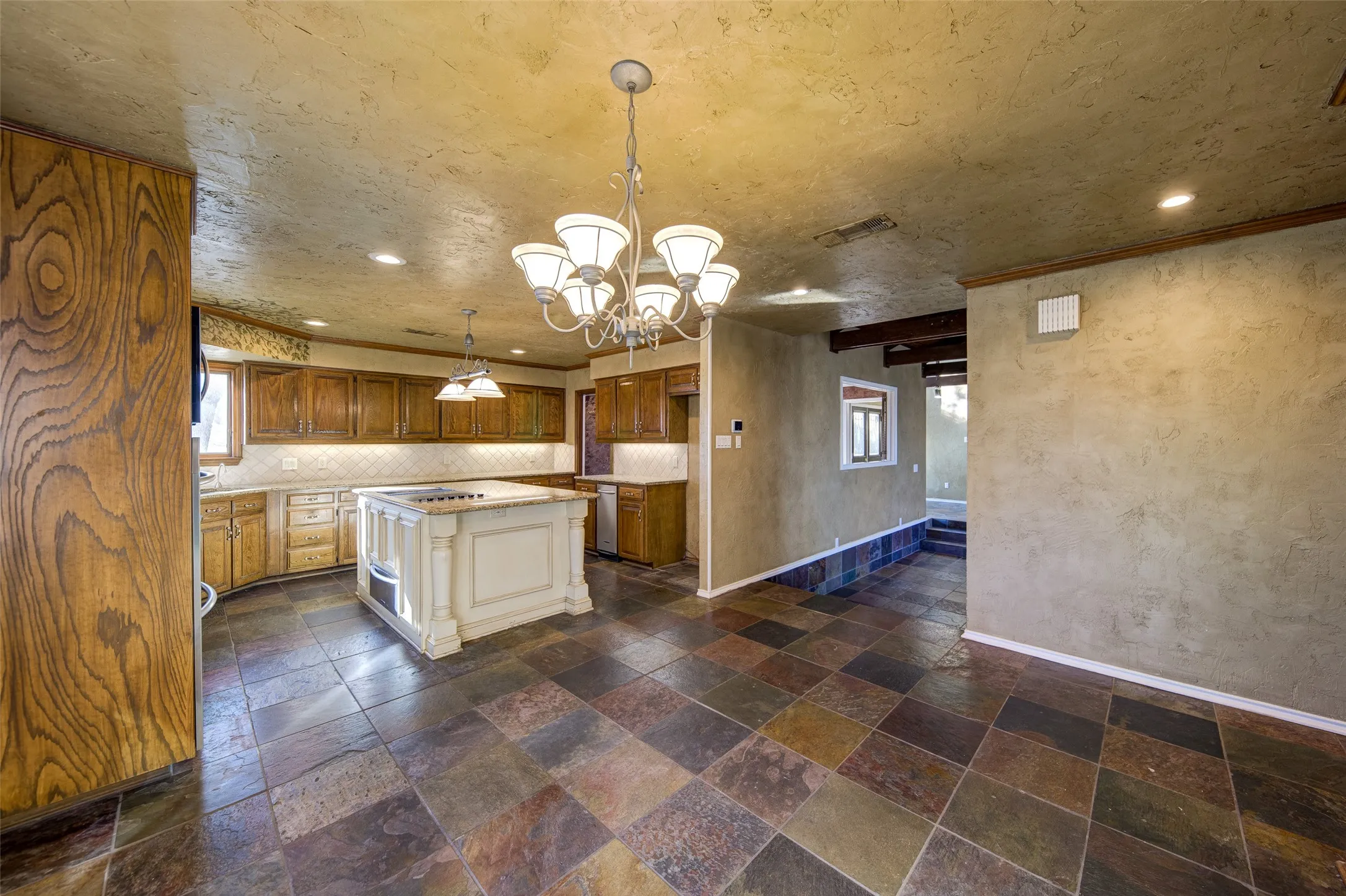 Kitchen with stone tile flooring, light countertops, a chandelier, brown cabinets, and recessed lighting