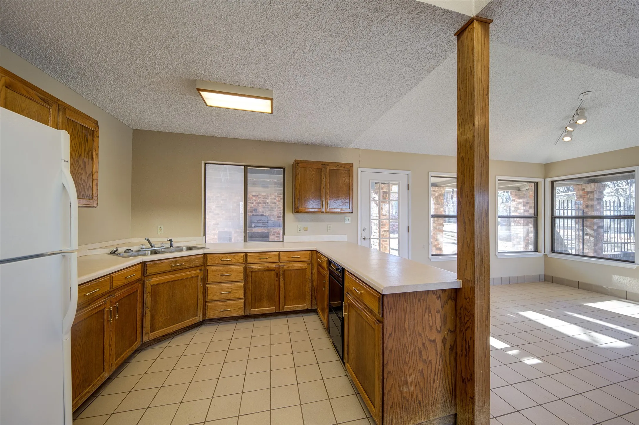 Kitchen featuring freestanding refrigerator, a textured ceiling, light countertops, light tile patterned floors, and a peninsula