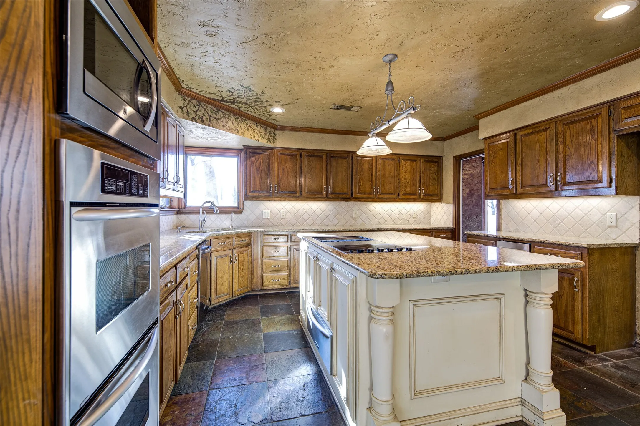 Kitchen featuring appliances with stainless steel finishes, stone tile floors, crown molding, a kitchen island, and light stone countertops