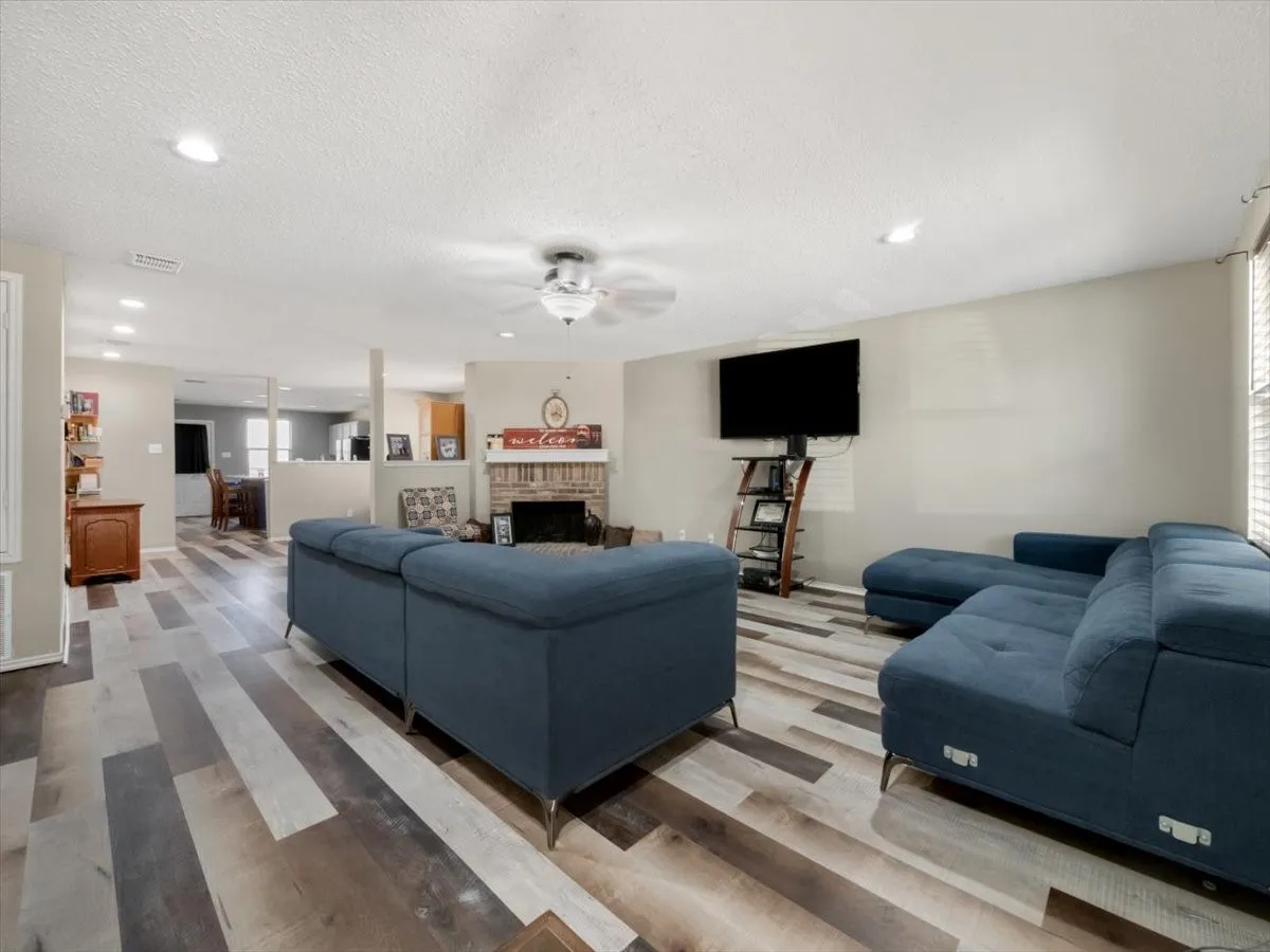 Living room with a textured ceiling, a brick fireplace, hardwood / wood-style floors, and ceiling fan