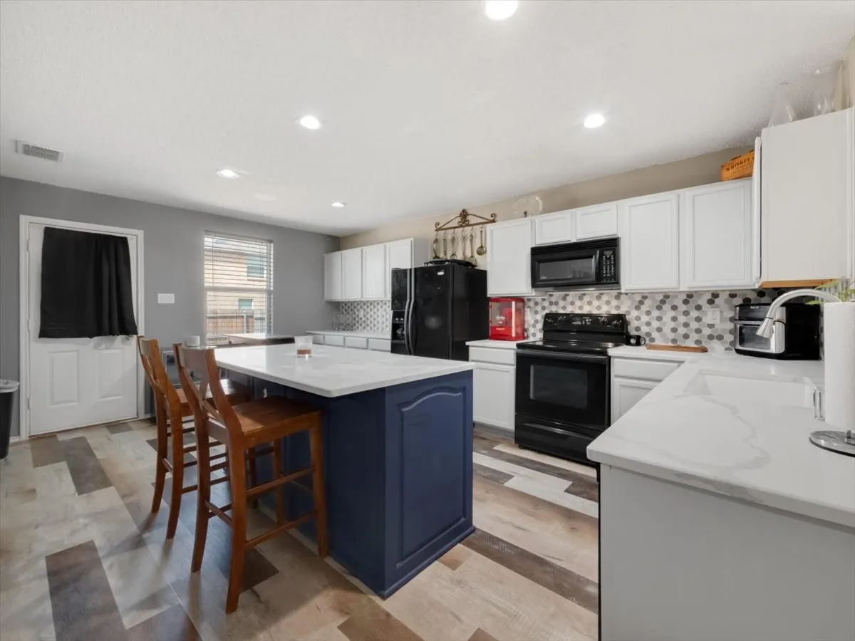 Kitchen with a kitchen island, backsplash, white cabinets, and black appliances
