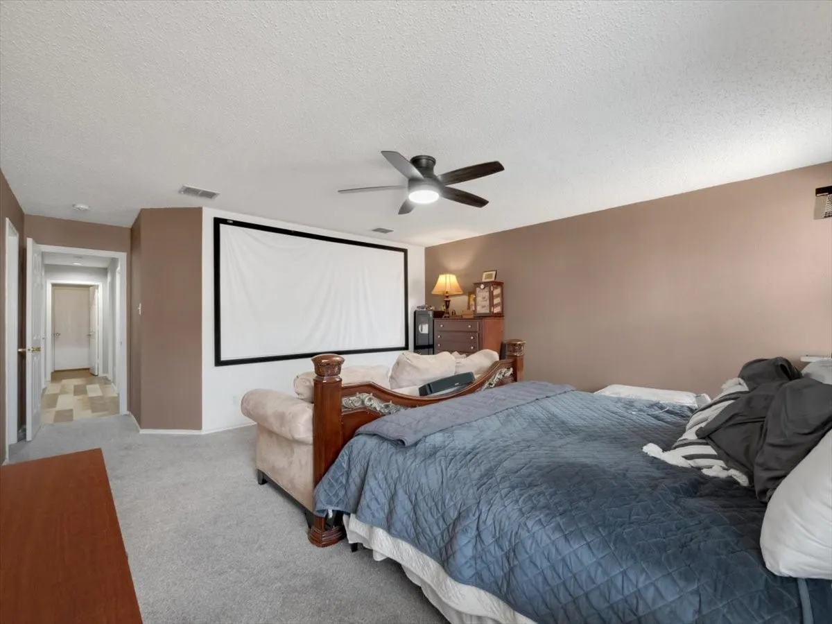 Bedroom with ceiling fan, a textured ceiling, and light carpet
