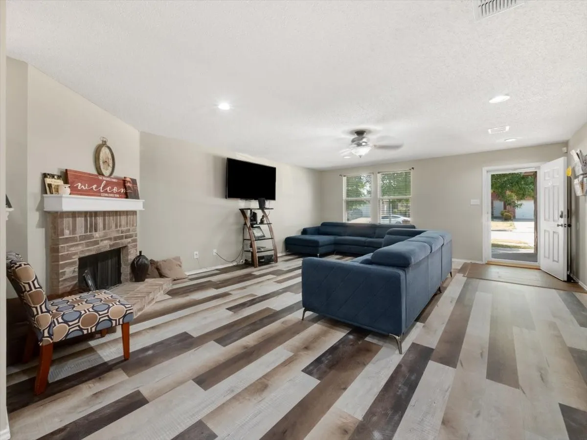 Living room featuring a brick fireplace, a textured ceiling, hardwood / wood-style flooring, and ceiling fan