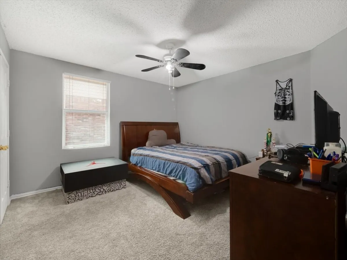 Bedroom with ceiling fan, light colored carpet, and a textured ceiling