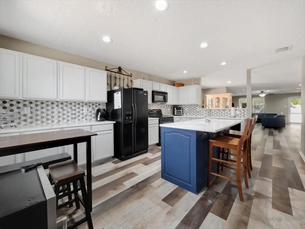 Kitchen with a textured ceiling, black appliances, a center island, a kitchen bar, and white cabinetry