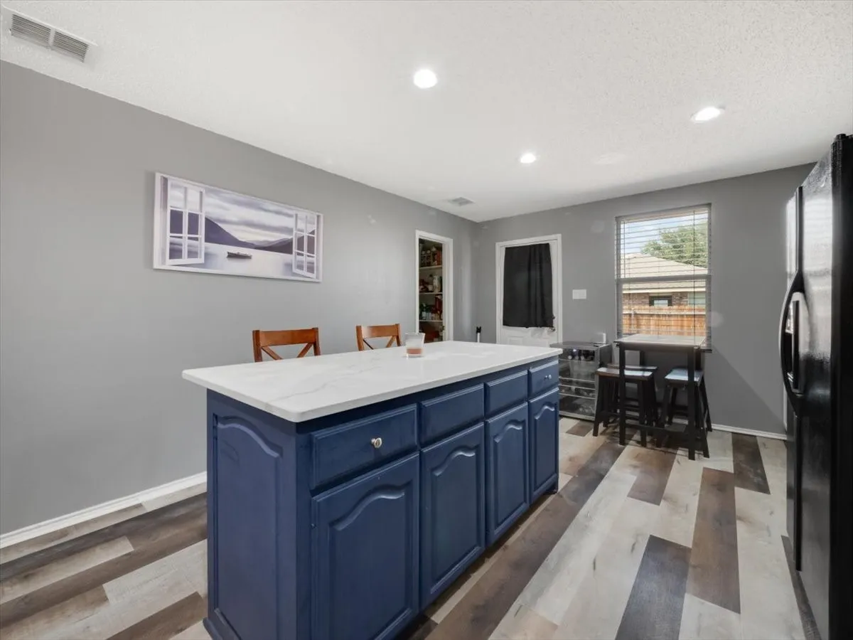 Kitchen featuring light hardwood / wood-style floors, black fridge, blue cabinets, a textured ceiling, and a center island