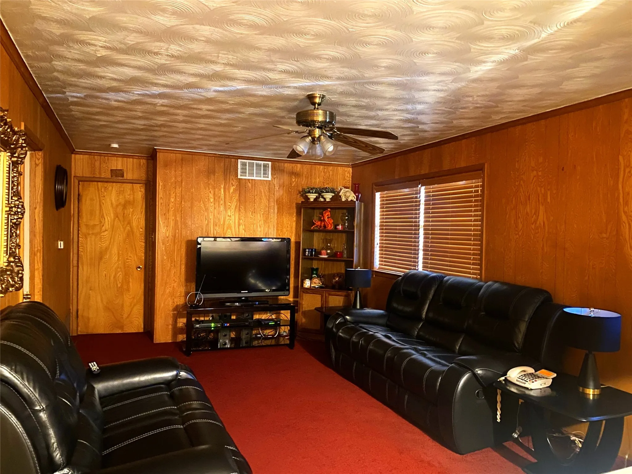 Carpeted living room featuring a textured ceiling, ceiling fan, crown molding, and wooden walls