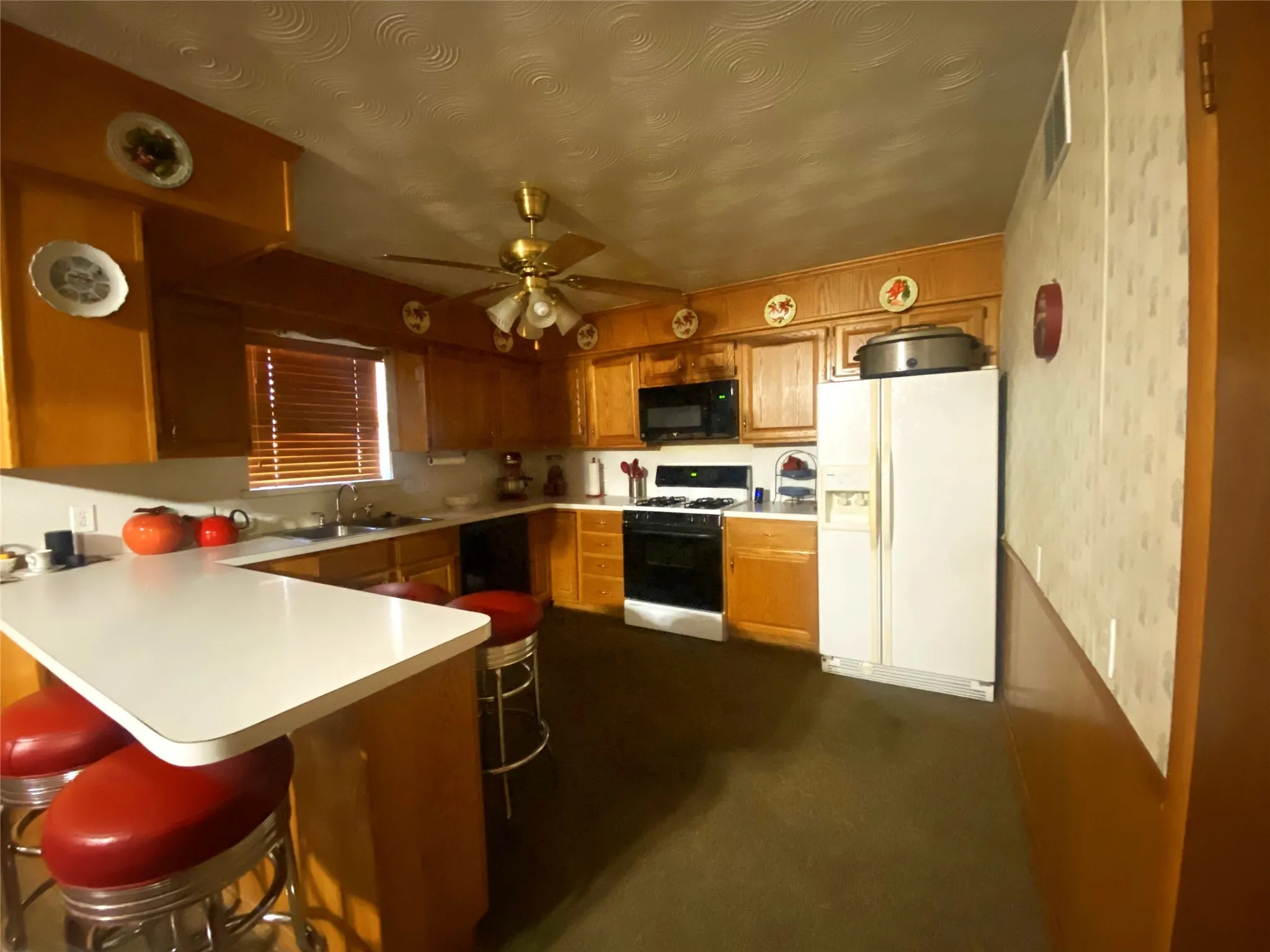 Kitchen featuring gas stove, kitchen peninsula, a kitchen bar, sink, and white fridge with ice dispenser