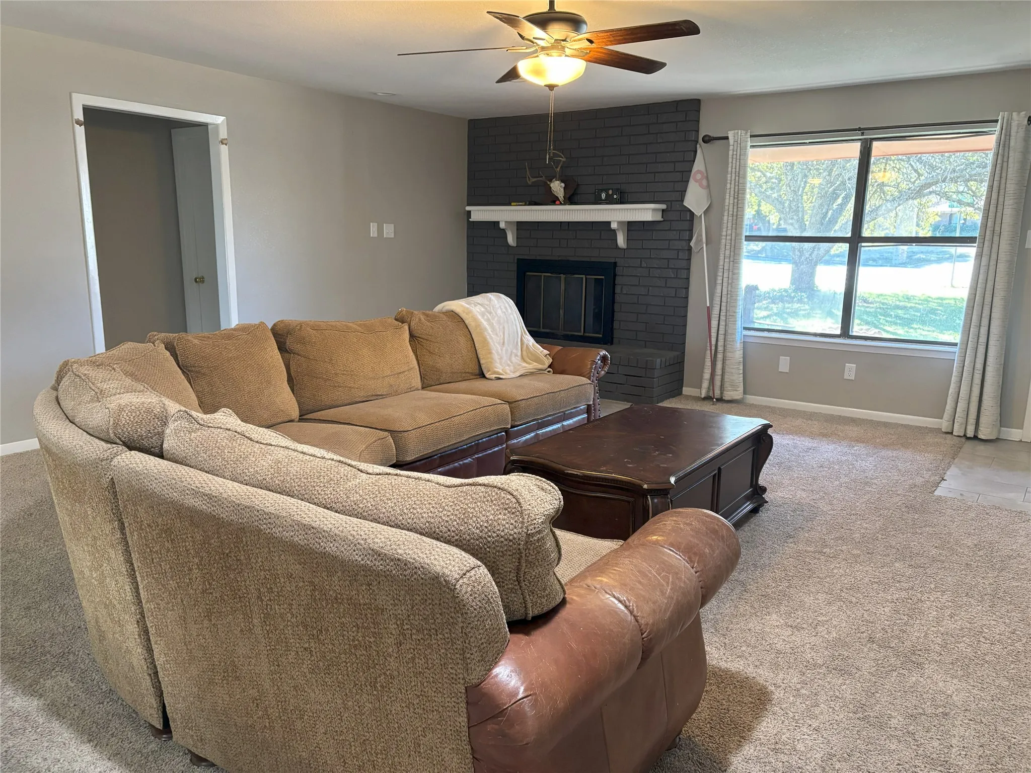 Living room with carpet flooring, ceiling fan, and a brick fireplace