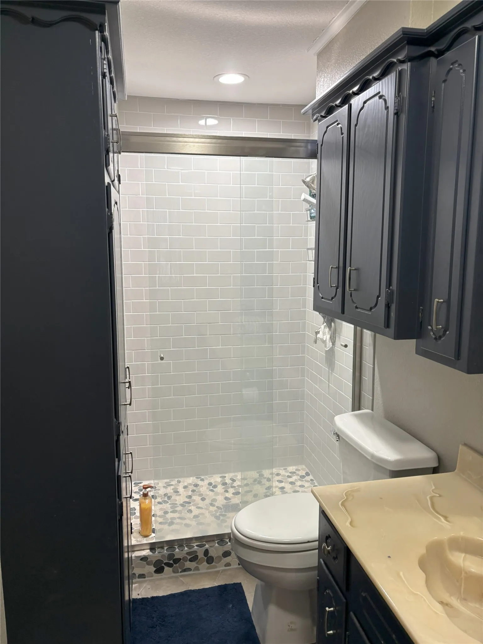 Bathroom with a tile shower, tile patterned floors, a textured ceiling, toilet, and vanity