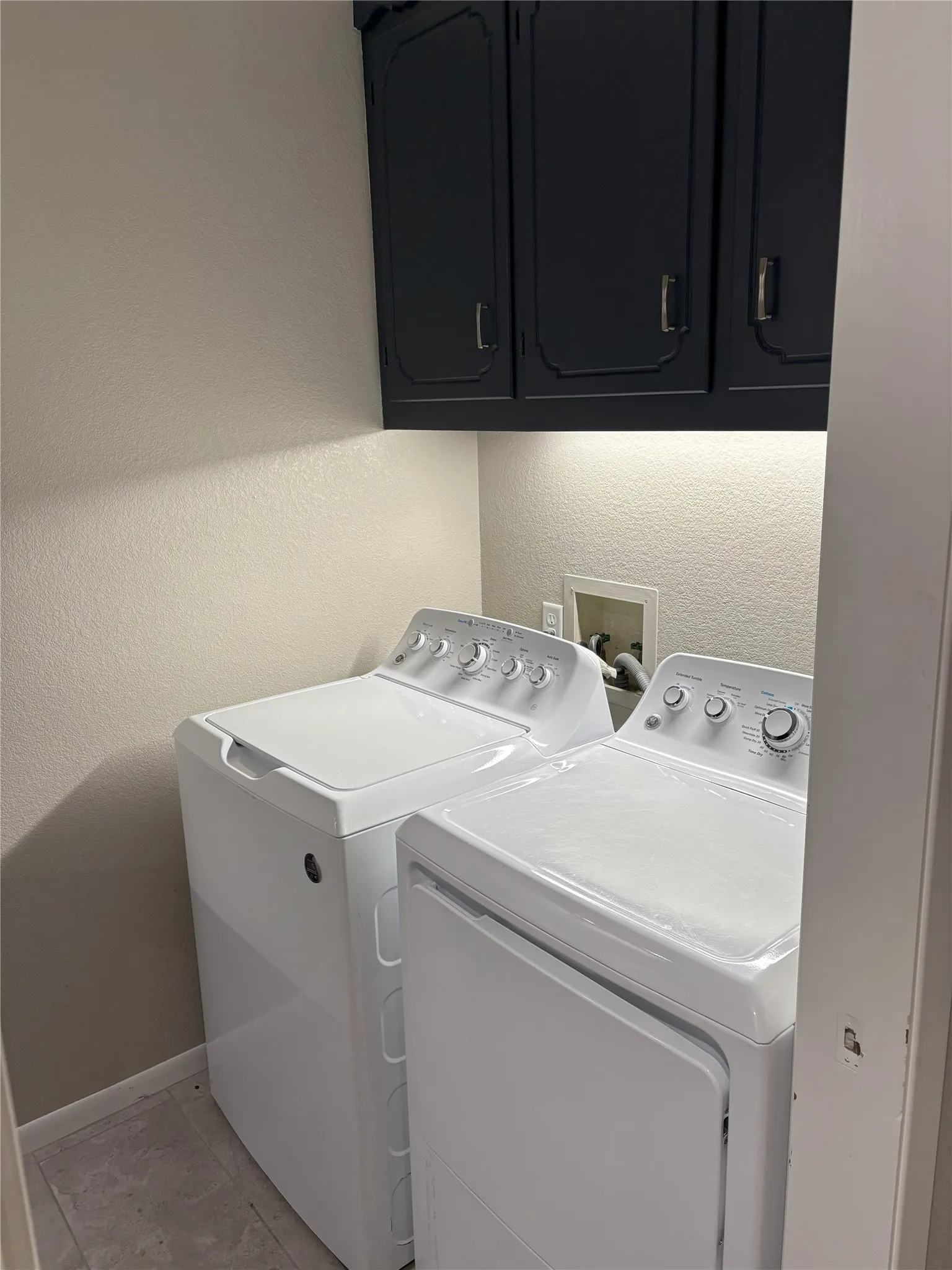 Clothes washing area featuring cabinets, light tile patterned floors, and washing machine and clothes dryer