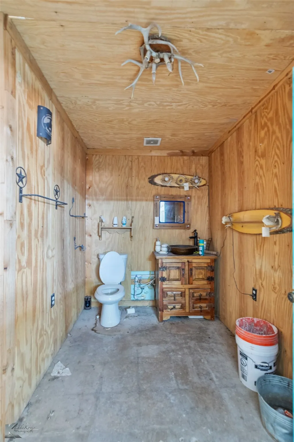 Bathroom featuring wood ceiling, toilet, concrete floors, and wood walls