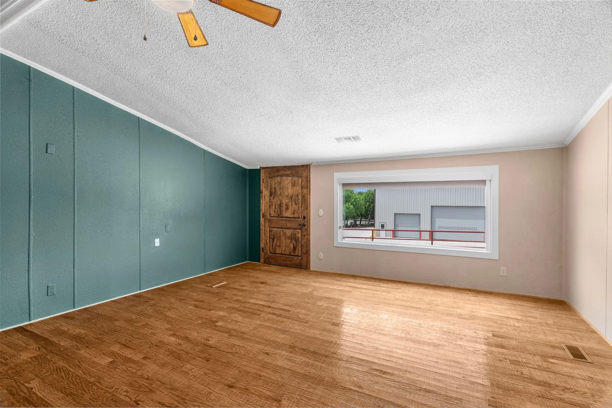 Unfurnished room featuring hand scraped wood floors, picture window overlooking warehouse and crown molding