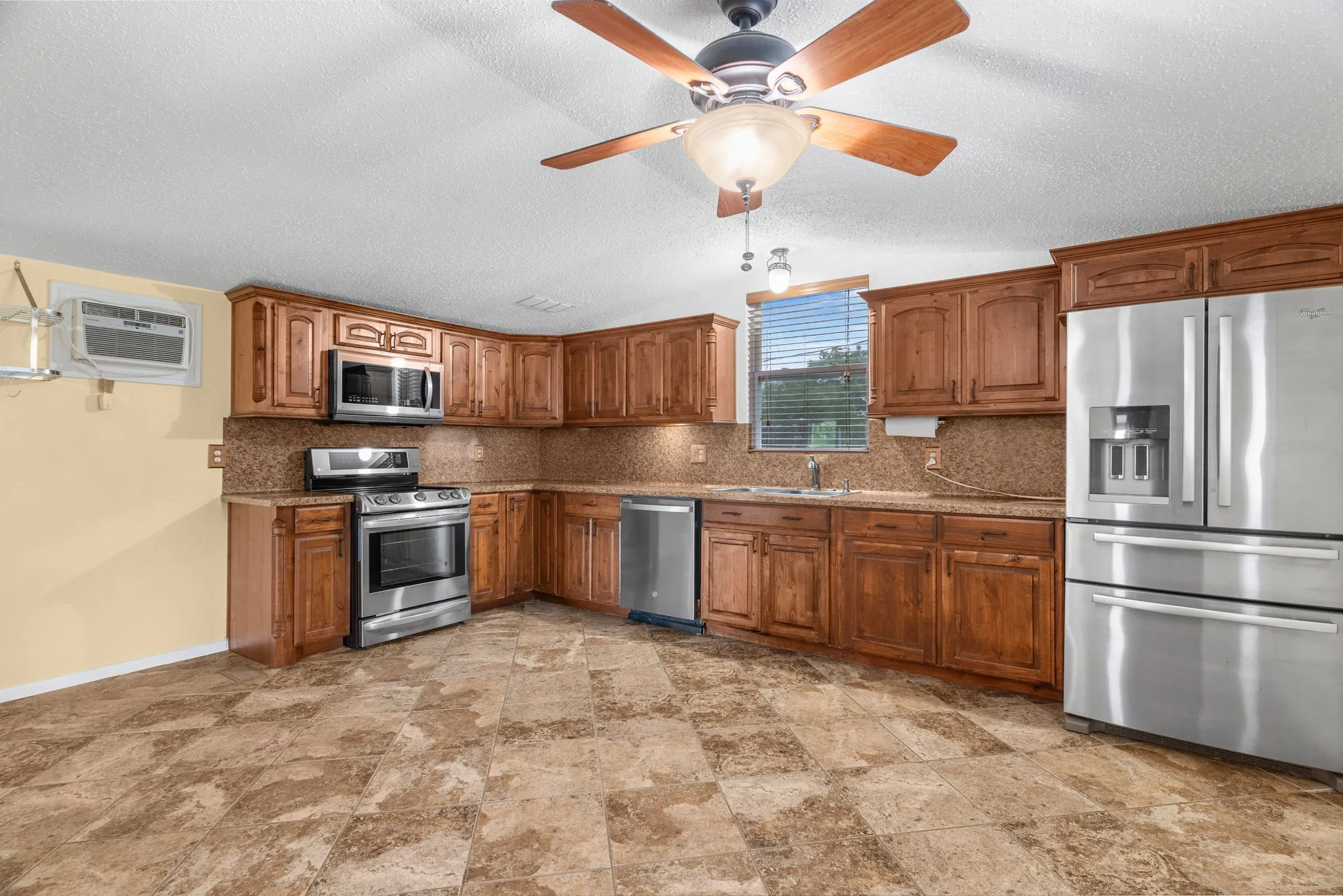 Kitchen with appliances with stainless steel finishes, brown cabinetry, and decorative backsplash