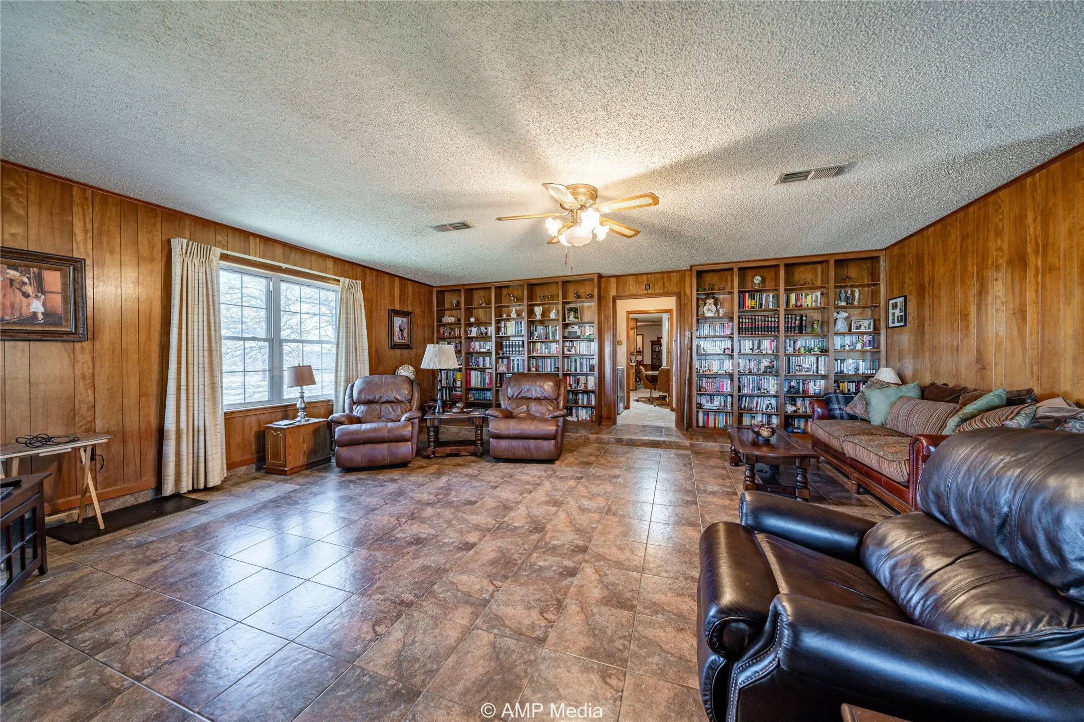 Living room with ceiling fan, a textured ceiling, and wood walls