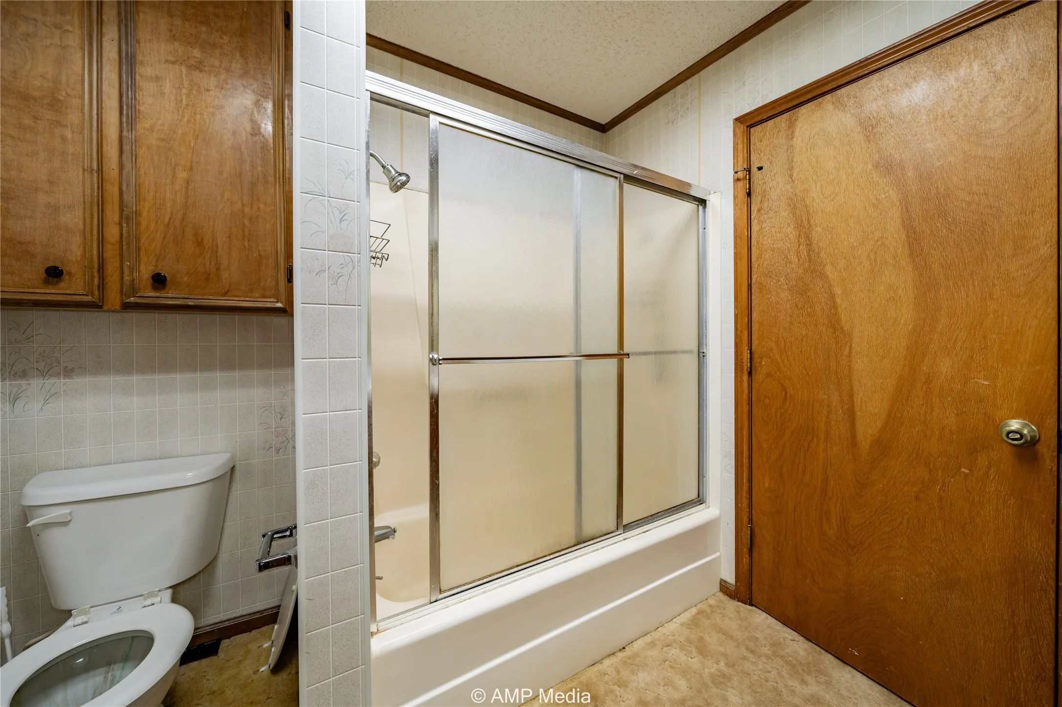 Bathroom with tile walls, bath / shower combo with glass door, ornamental molding, a textured ceiling, and toilet